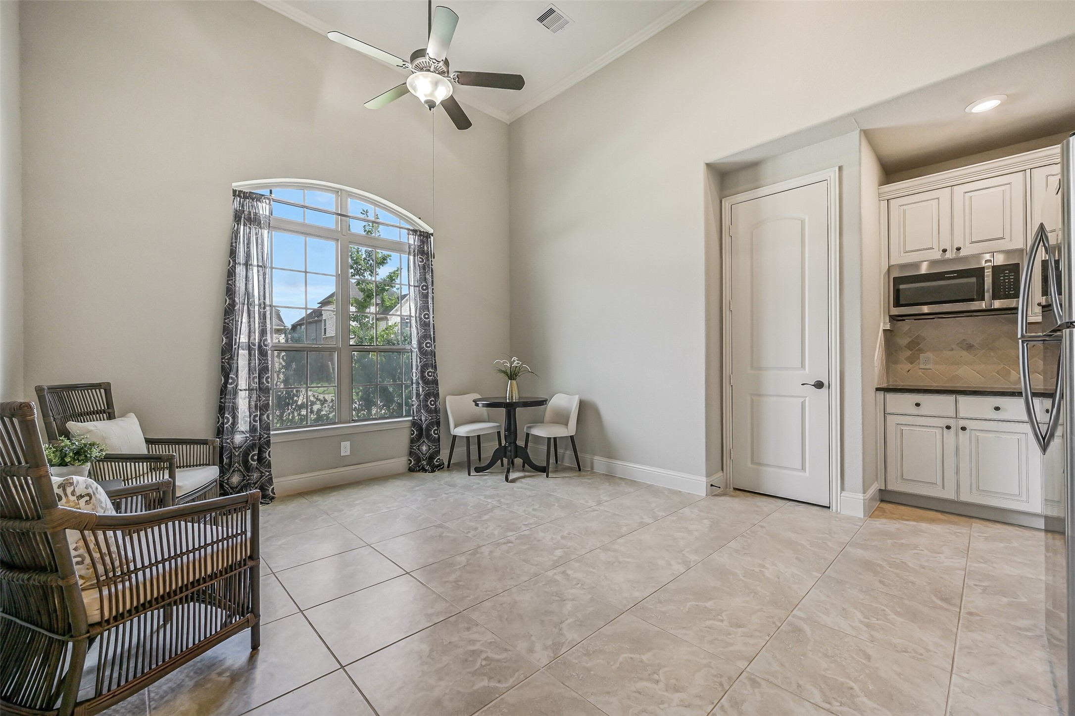 The apartment's spacious living area features a soaring 14' ceiling, crown molding, tile flooring & a lighted ceiling fan. A large arched window welcomes natural light, while the nearby kitchenette makes this a comfortable, self-contained living space. The door beside the kitchenette opens to a utility closet with connections for a stackable washer & dryer.