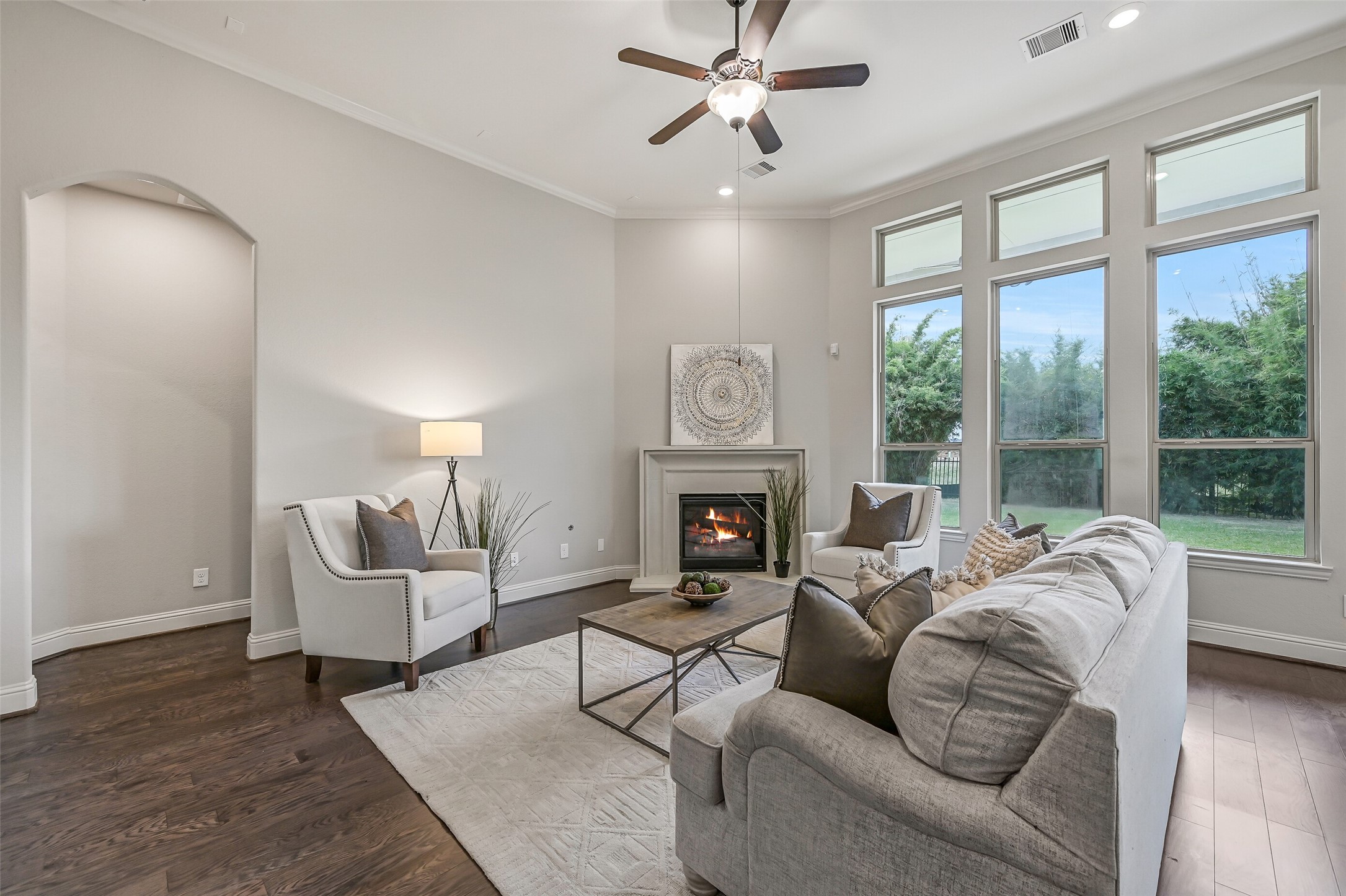 Another look at the welcoming family room, where the cast-stone gas-log fireplace anchors the space and tall windows bring in beautiful natural light. Rich luxury vinyl plank flooring, crown molding & a lighted ceiling fan complete the room.