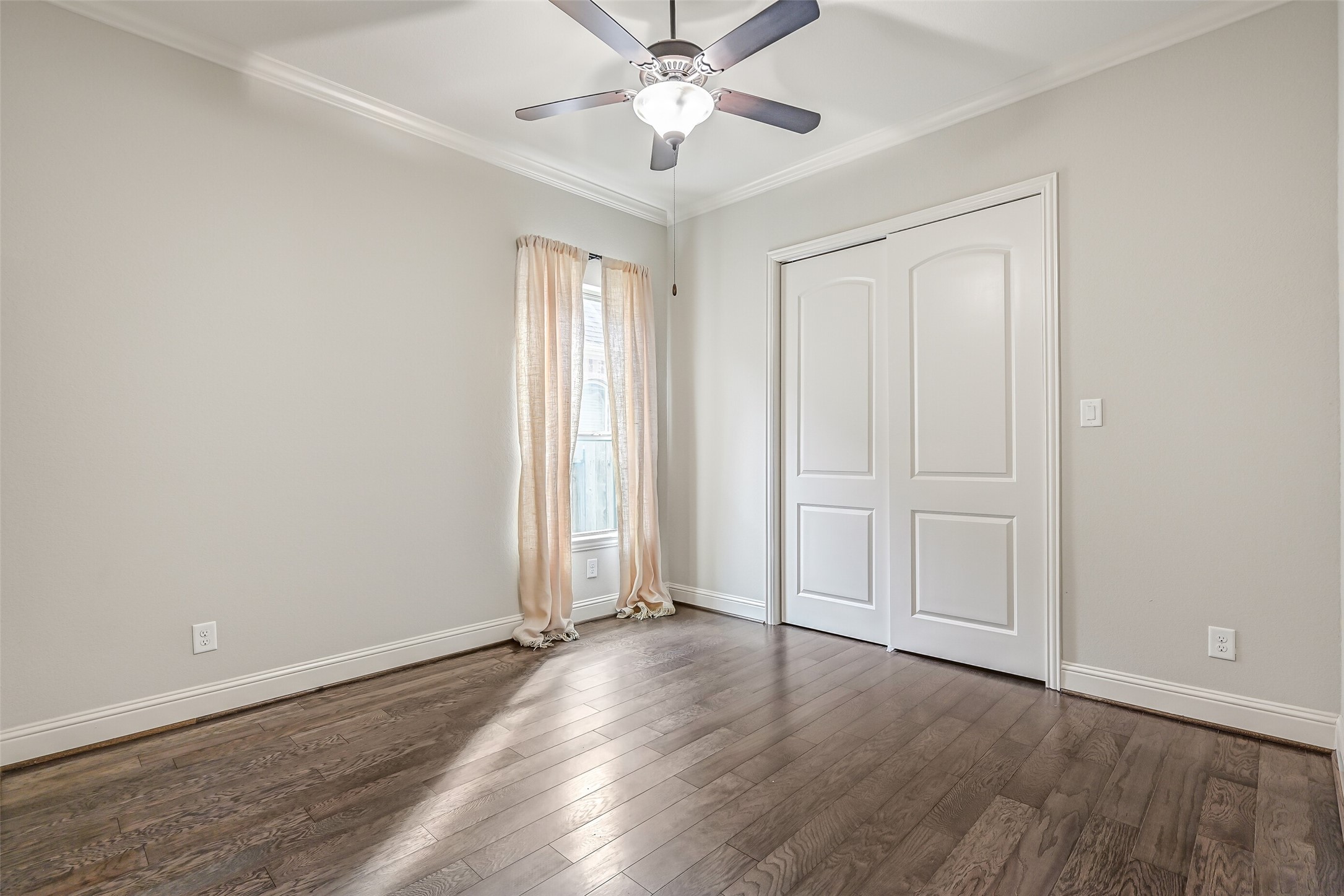 The apartment's separate bedroom offers luxury vinyl plank flooring, crown molding, a lighted ceiling fan & a side-facing window with draperies. A generous sliding-door closet provides wardrobe storage, completing this thoughtfully arranged private living space.
