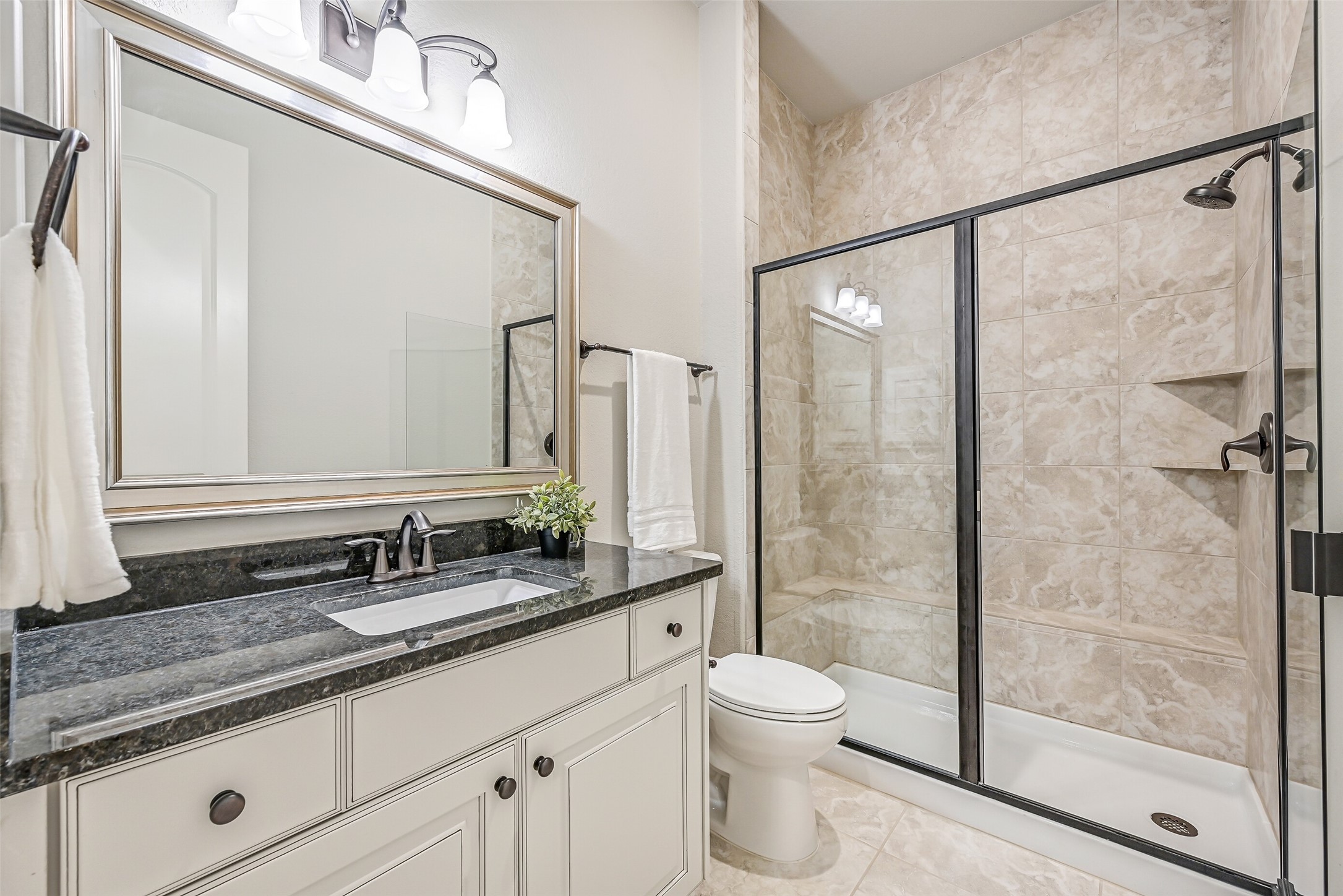 The apartment enjoys its own full bathroom with a granite-topped vanity, framed mirror, tile flooring & a glass-enclosed walk-in shower with tiled surround, built-in shaving ledge & corner shelving. Conveniently accessible from the living area as well as the bedroom.
