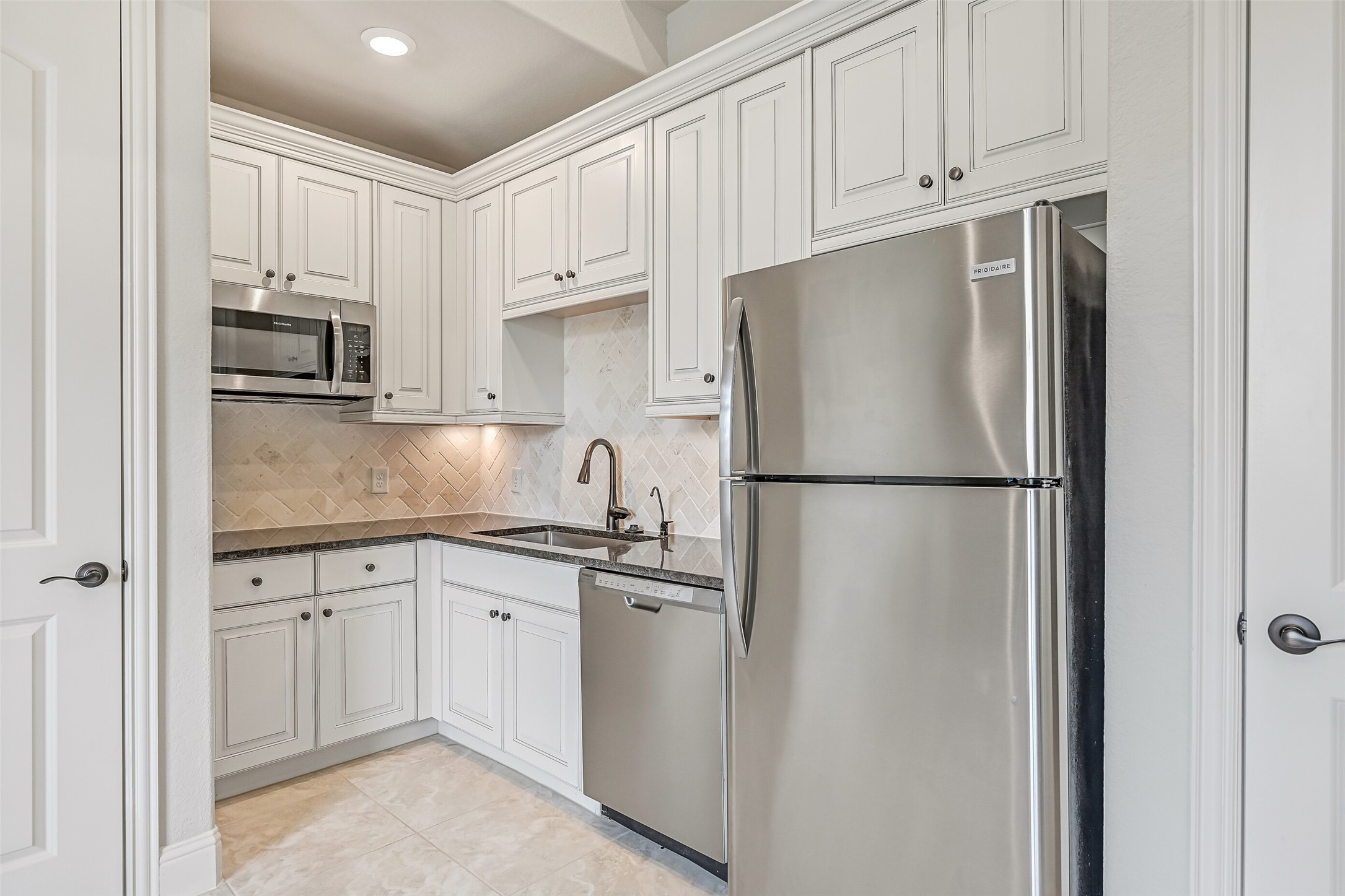 Don't let the word kitchenette fool you! This well-equipped space features granite countertops, white raised-panel cabinetry, a herringbone tile backsplash, undercabinet lighting, stainless Frigidaire dishwasher, microwave & full-size refrigerator. A deep single-basin sink & pantry add even more functionality.