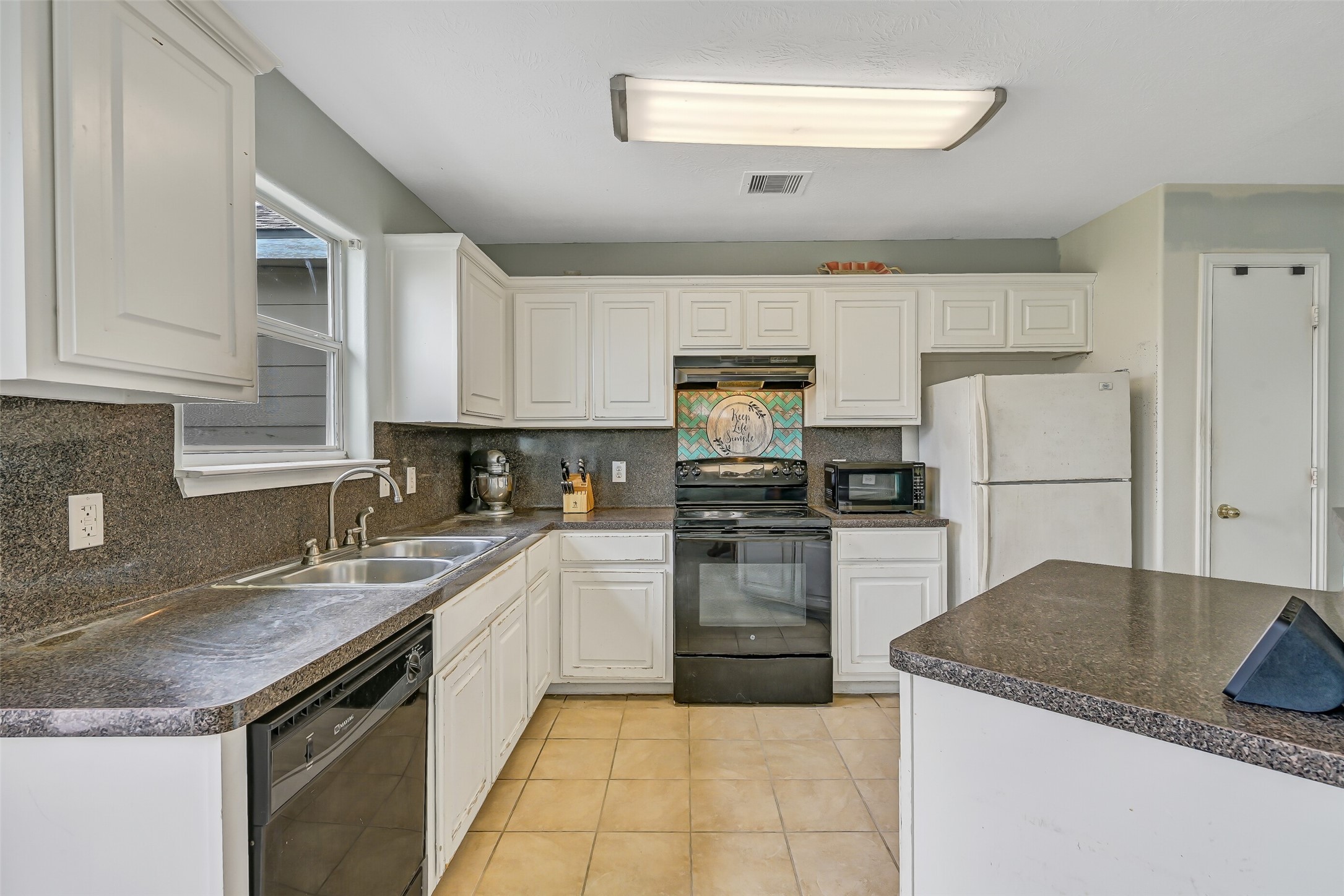Another view of the kitchen highlights the wraparound workspace, breakfast bar, electric range, dishwasher, and ample upper and lower cabinetry.