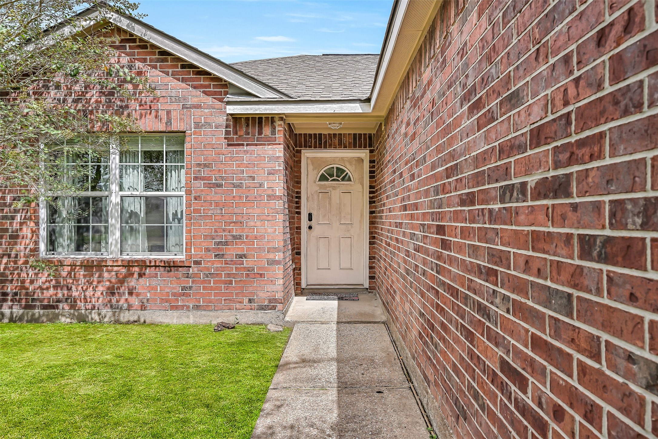 A brick-lined walkway leads to the recessed front entry, creating a sheltered approach to this single-story home.