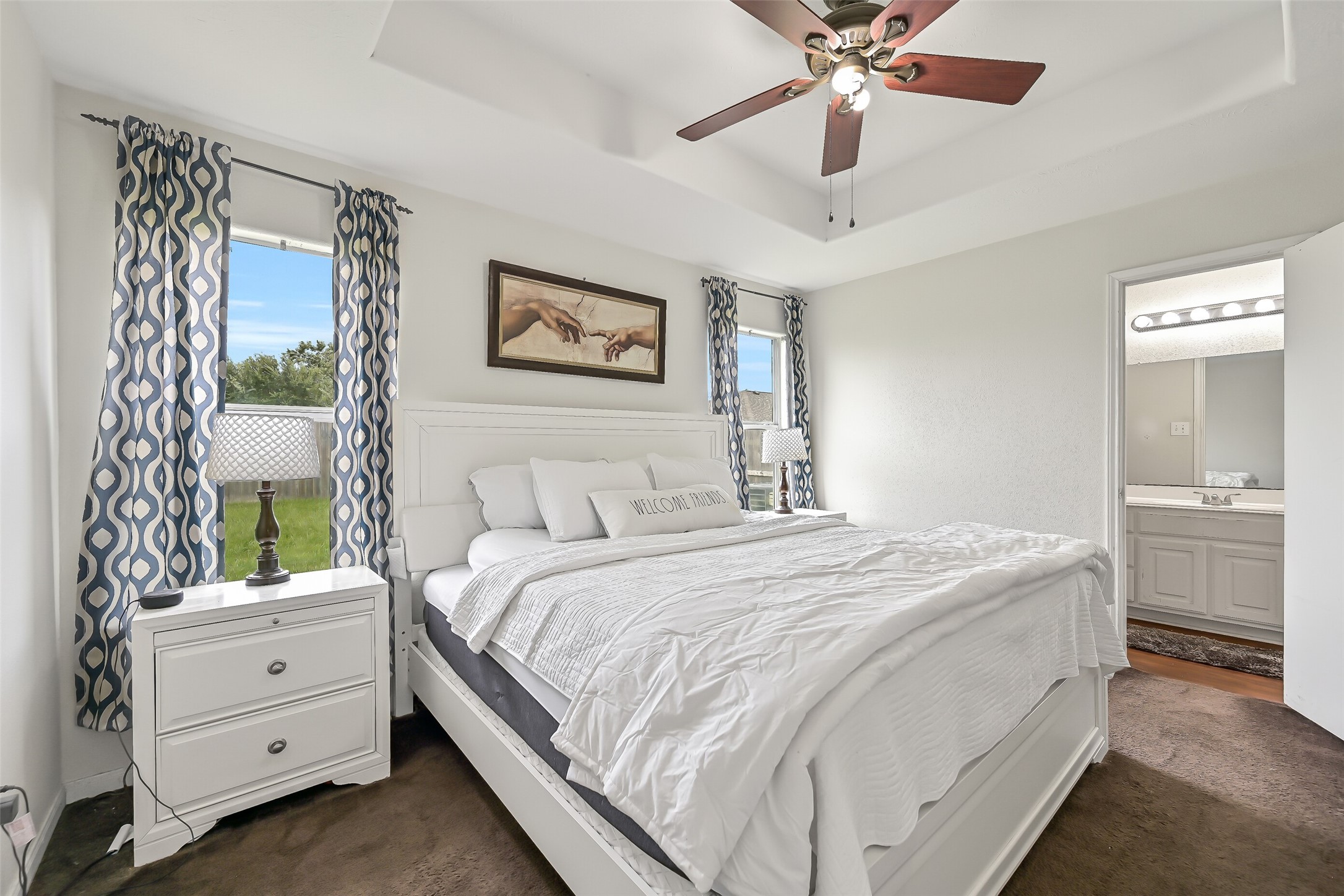 The primary bedroom offers a spacious retreat with a tray ceiling, ceiling fan, and two windows that fill the room with natural light. A private en suite bath completes the suite.
