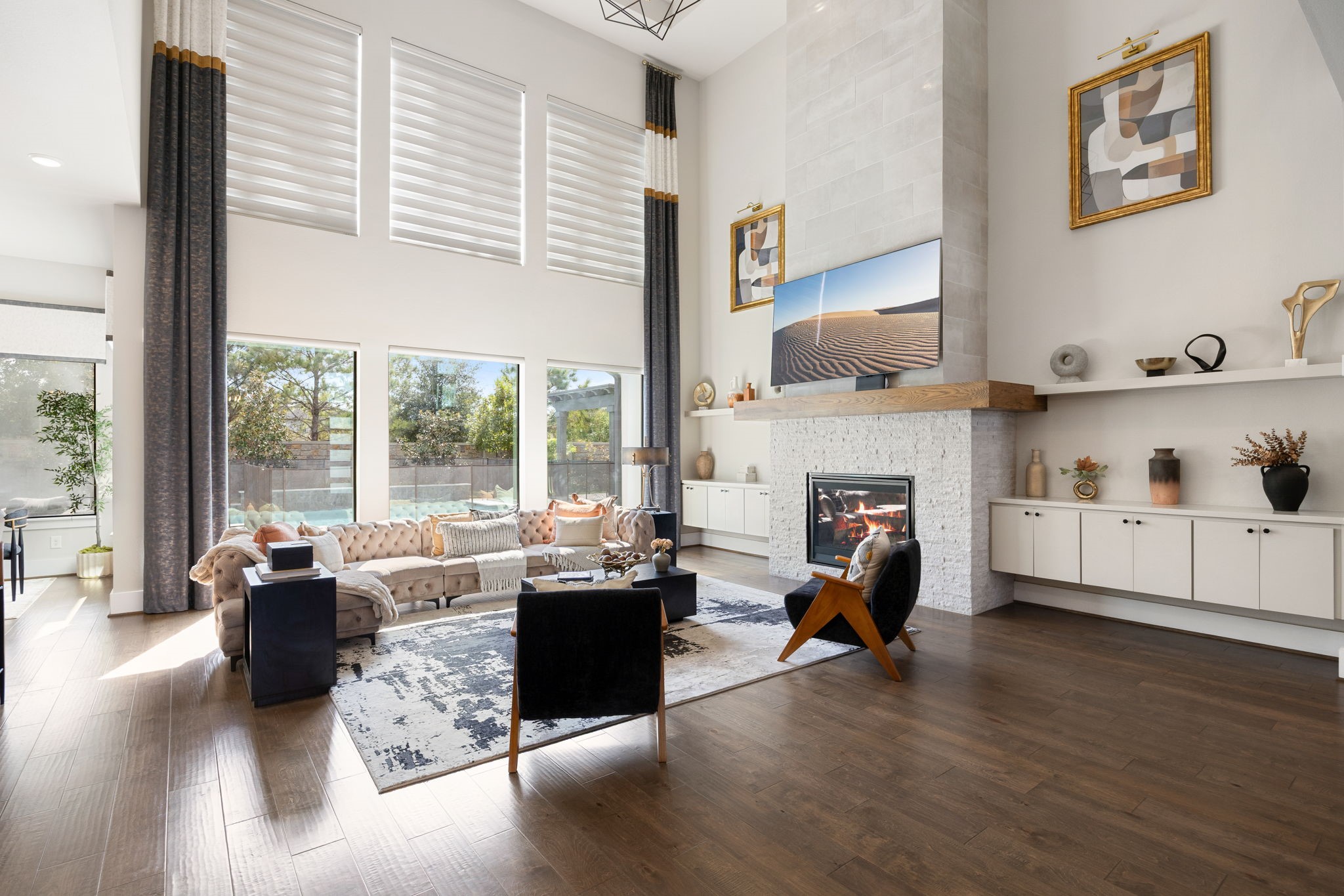 Enjoy an abundance of natural light in this spacious living area with beautiful views of the backyard. Additional upgrades include floating cabinetry, shelving for storage and decor, tray ceiling, and custom drapery and lighting.
