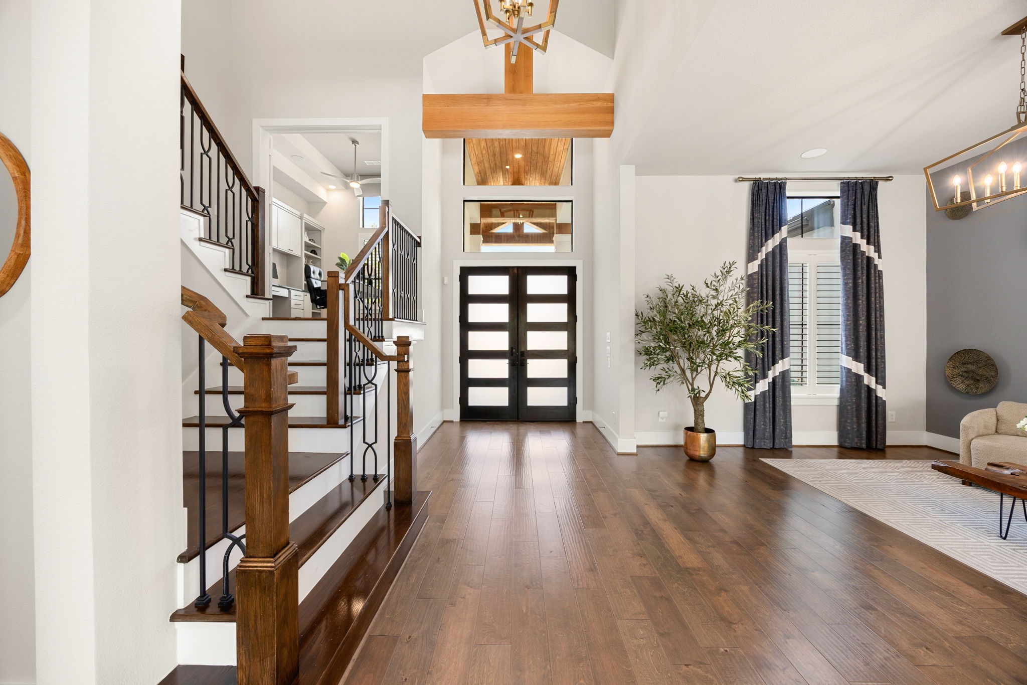 Step inside to a breathtaking entryway featuring soaring ceilings, beautiful engineered hardwood flooring, custom lighting, tall windows bringing in natural light, and an elegant staircase.