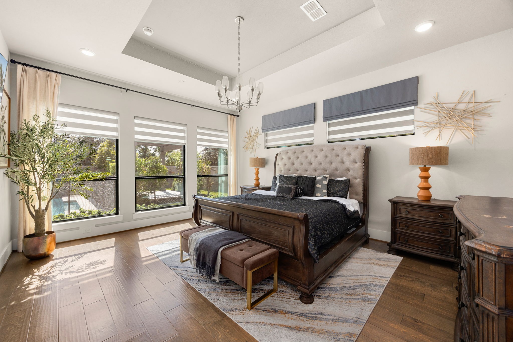 Spacious primary suite featuring a tray ceiling, large windows, custom shades, engineered wood floors, and a relaxing atmosphere.