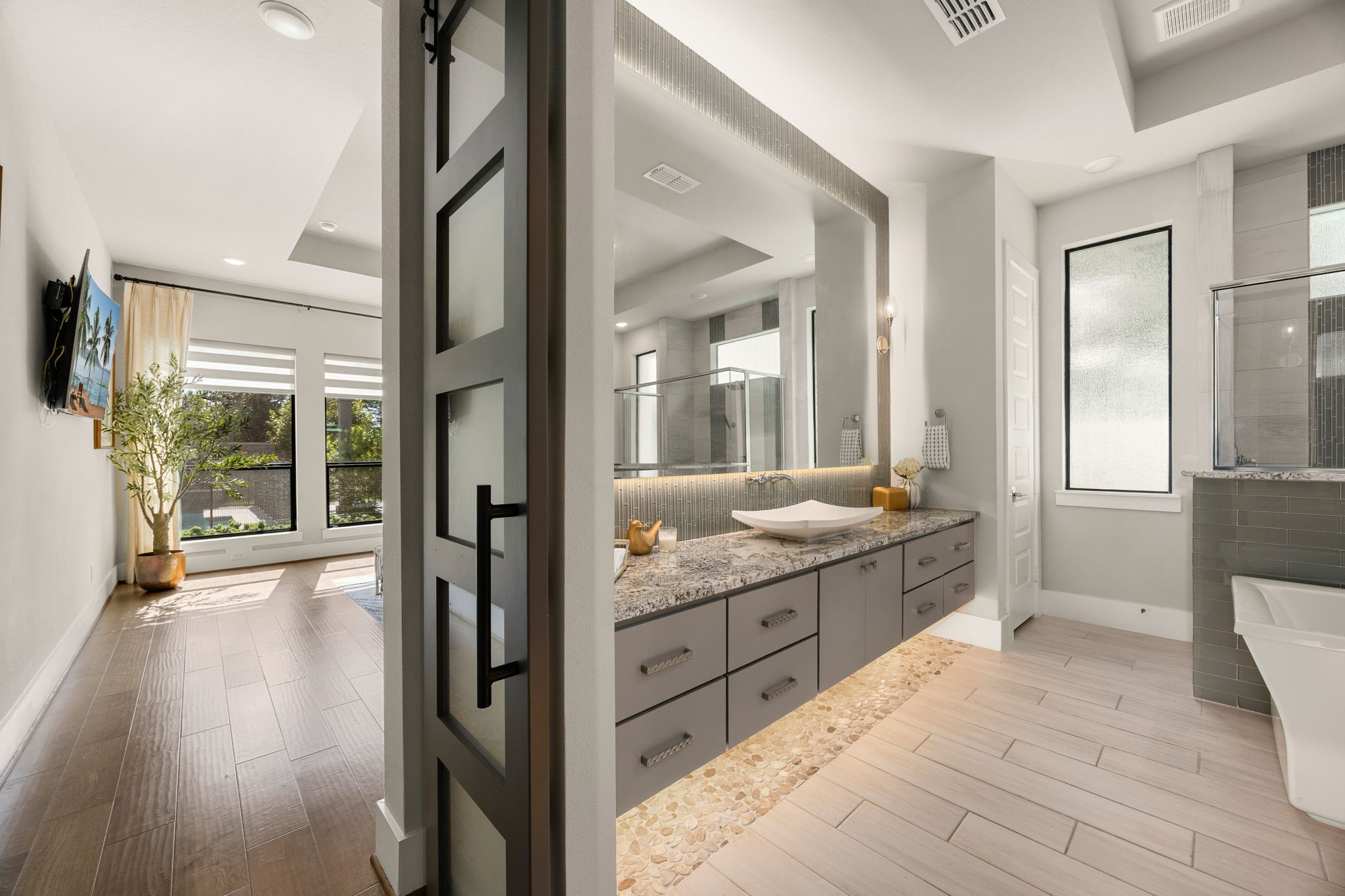 Luxurious primary bathroom featuring a sliding barn door, dual floating vanities, elegant finishes with mirror lighting and floor lighting, and a spacious, spa-inspired design.
