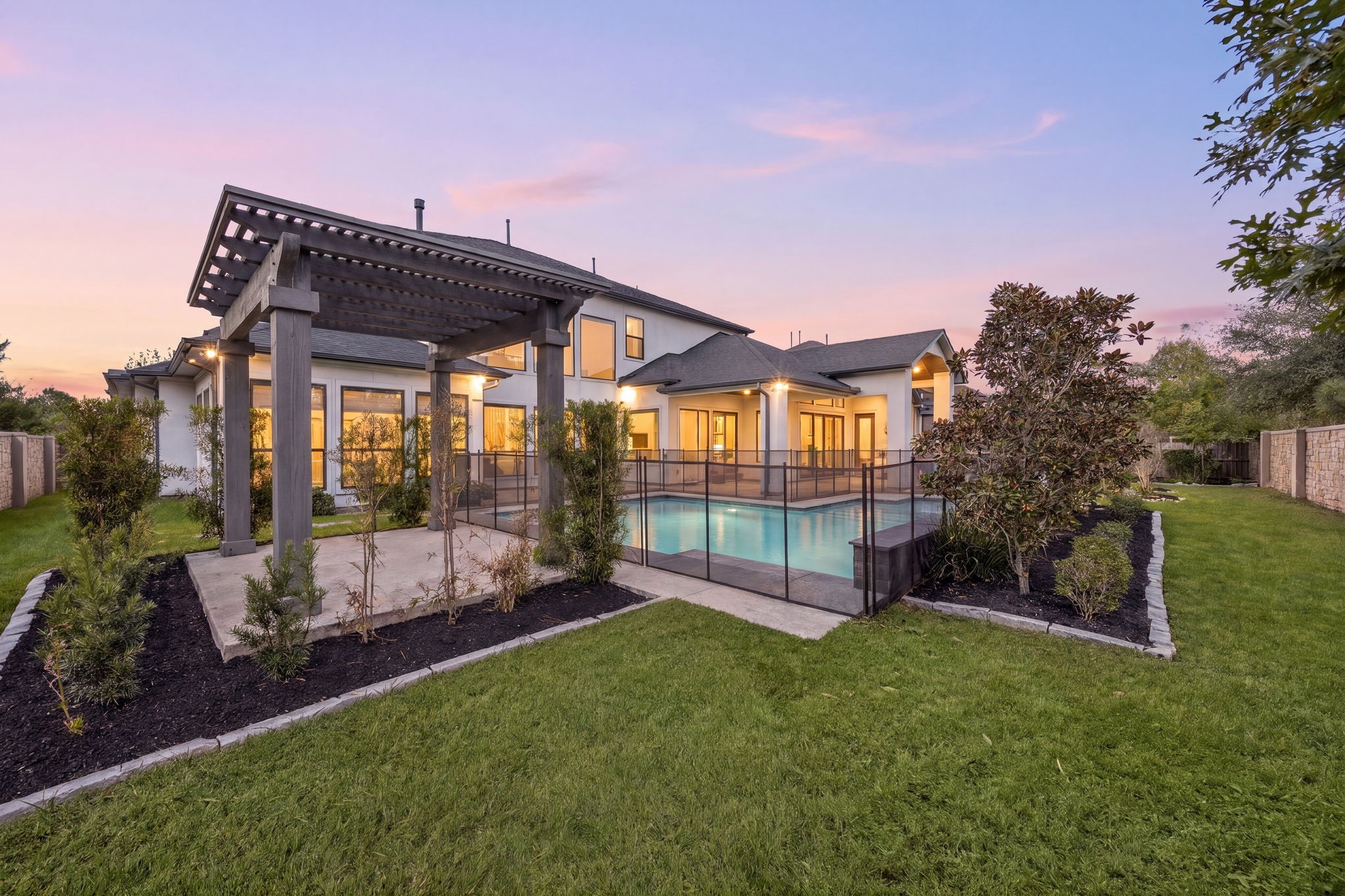Beautiful backyard retreat featuring a covered pergola, lush green lawn, and pool fence installed to keep the kids and pets safe.
