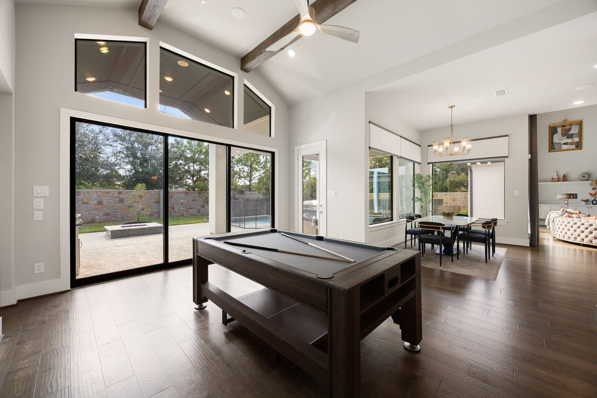 Spacious downstairs game room area with soaring ceilings and large sliding glass doors that overlook the backyard and connect to the kitchen and main living areas.