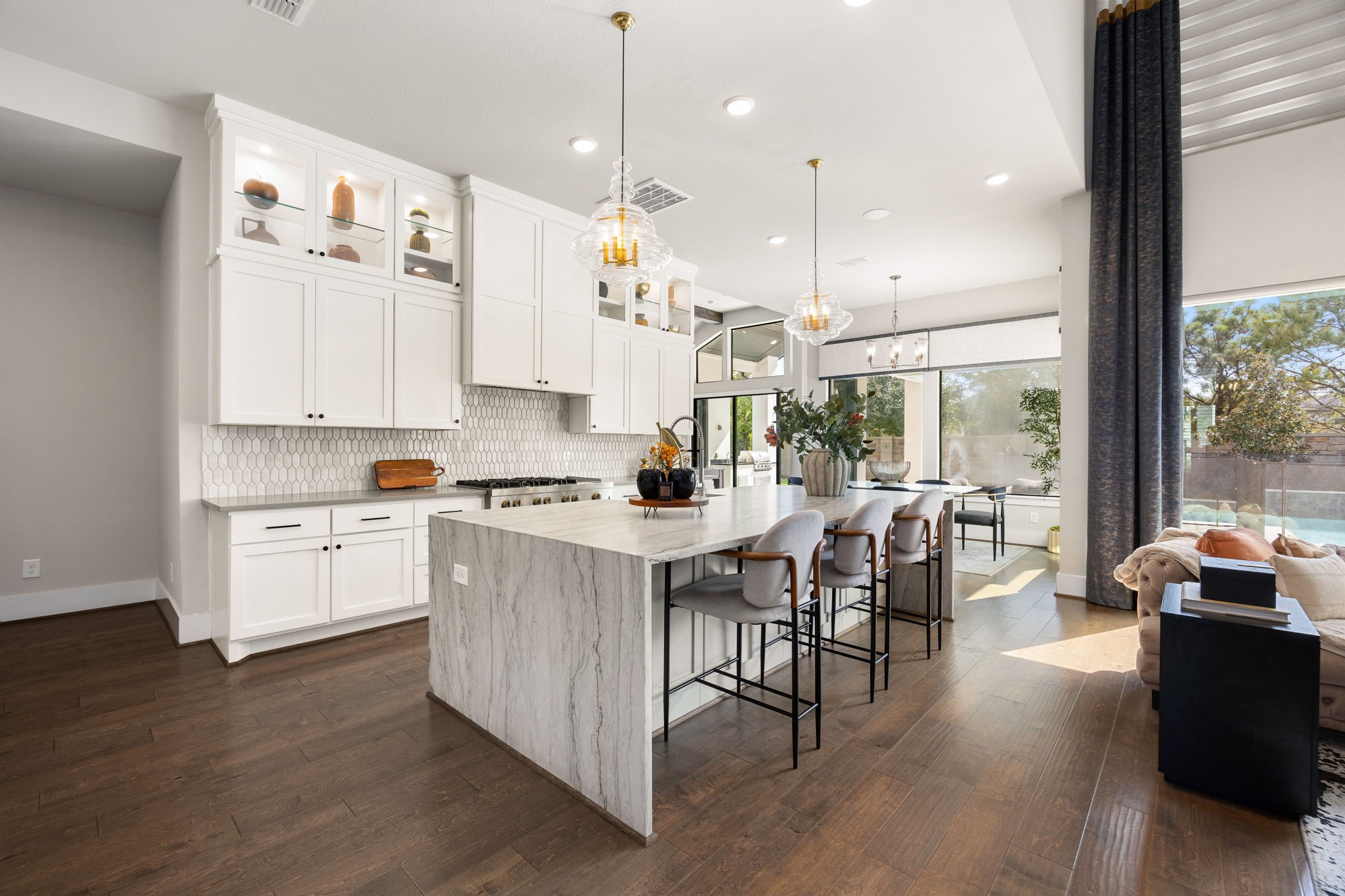 Gorgeous gourmet kitchen featuring a large center waterfall quartzite island, beautiful cabinetry to the ceiling with glass doors and shelves, and an open layout ideal for entertaining.