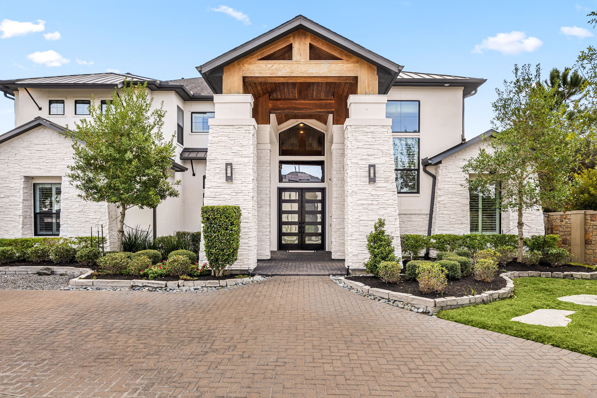 Grand front entrance with beautiful architectural details, stone bordered flower beds with landscape lighting, recessed soffit lighting, and pine ceiling with wood beams.