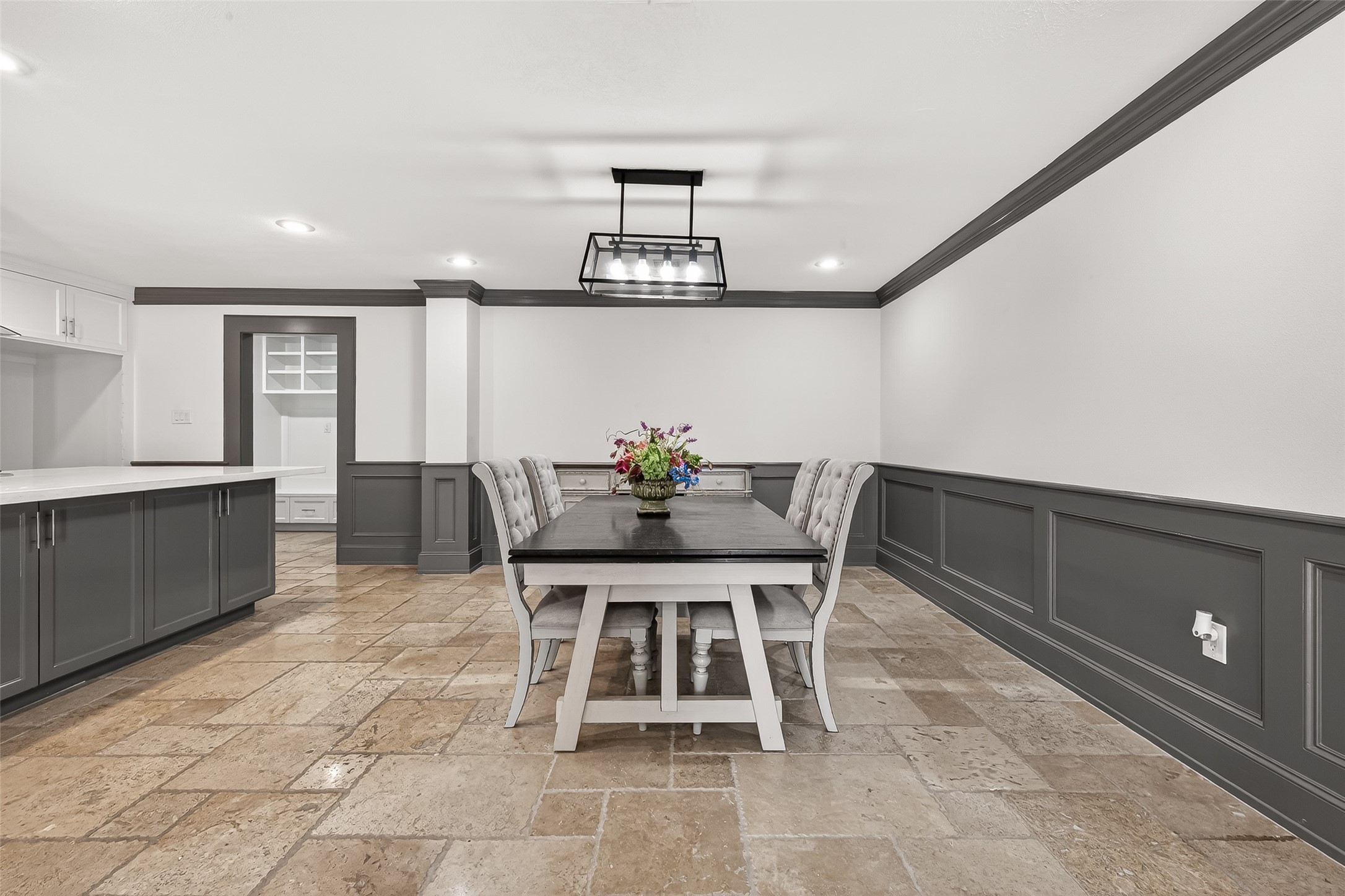 This dining area features elegant wainscoting and a modern light fixture. The room is complemented by a sleek, dark dining table and chairs, set on polished stone tiles.