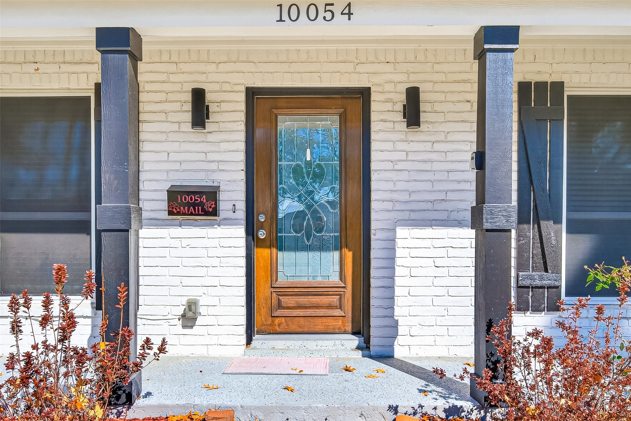 Front entrance with a white brick facade, a decorative wooden door with glass detailing, and dark wooden columns.