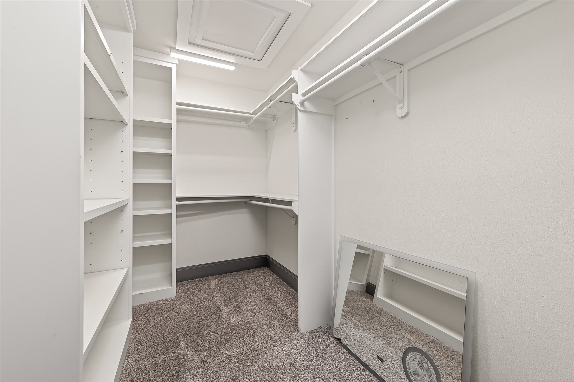 This is a walk-in closet with ample shelving and hanging space. It features carpeted flooring and a large mirror, perfect for organizing clothes and accessories.
