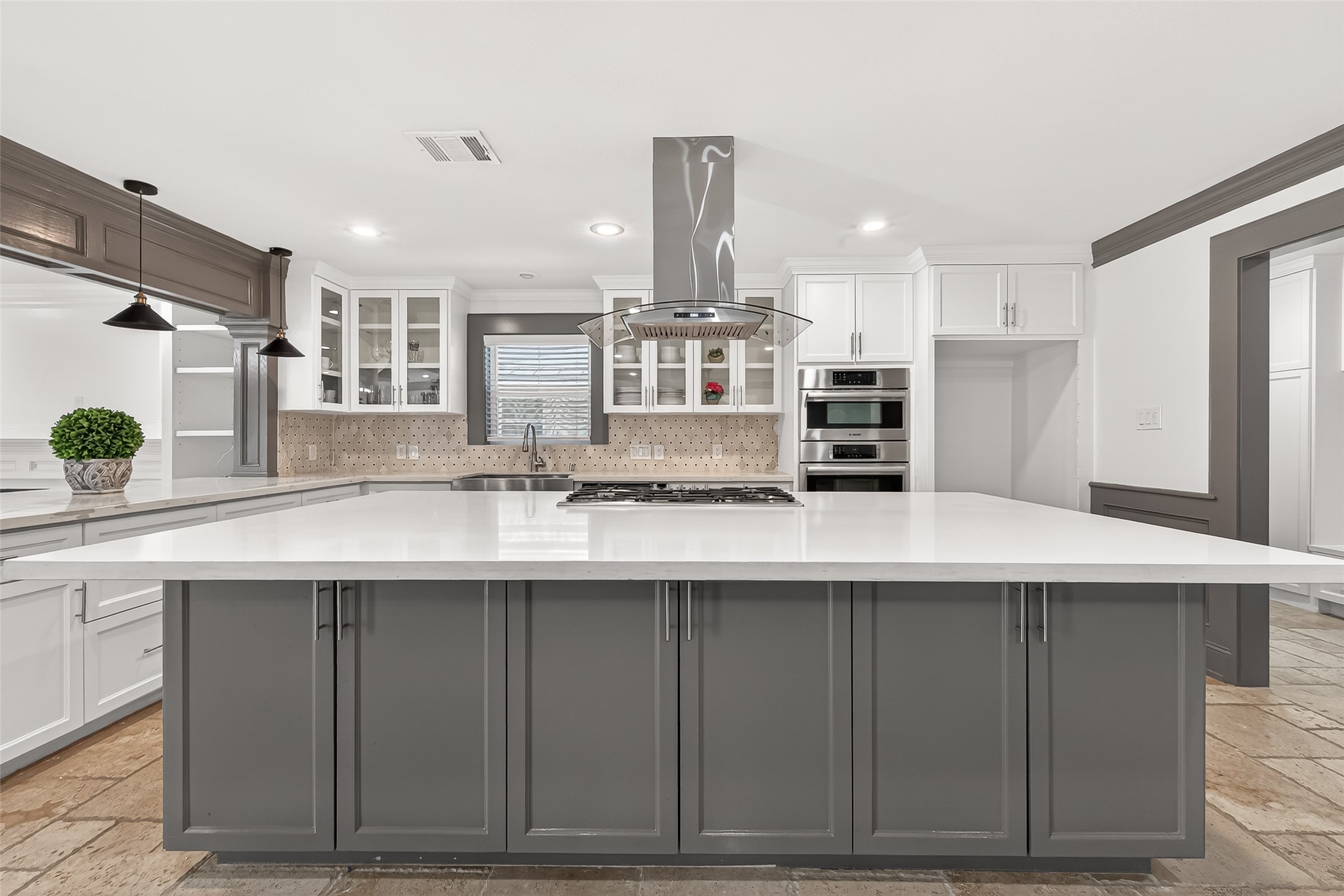 This modern kitchen features island with sleek gray cabinetry, a white countertop, and a built-in cooktop.