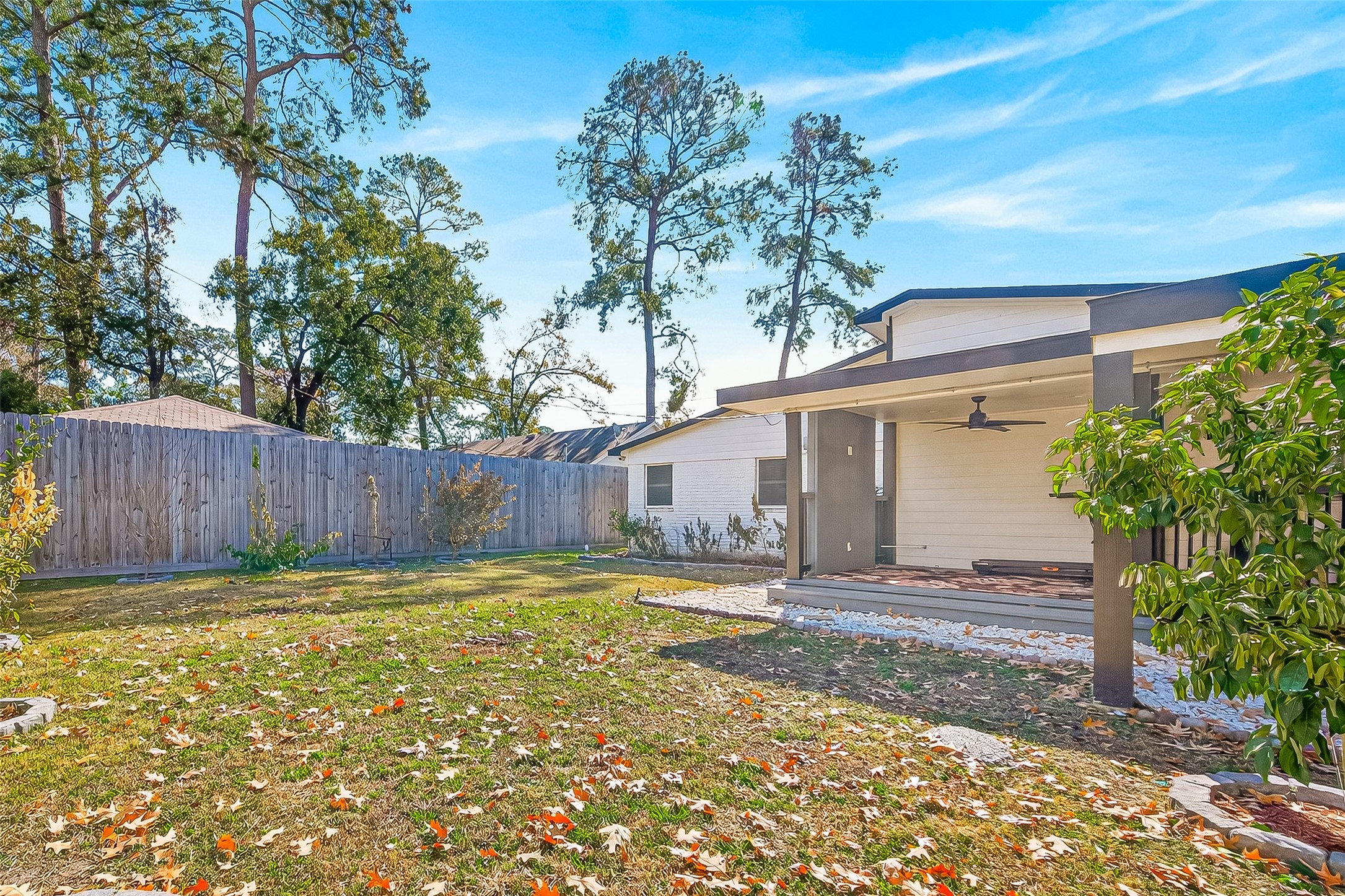 The yard is enclosed by a wooden fence, offering privacy, and is complemented by mature trees and a well-maintained lawn.