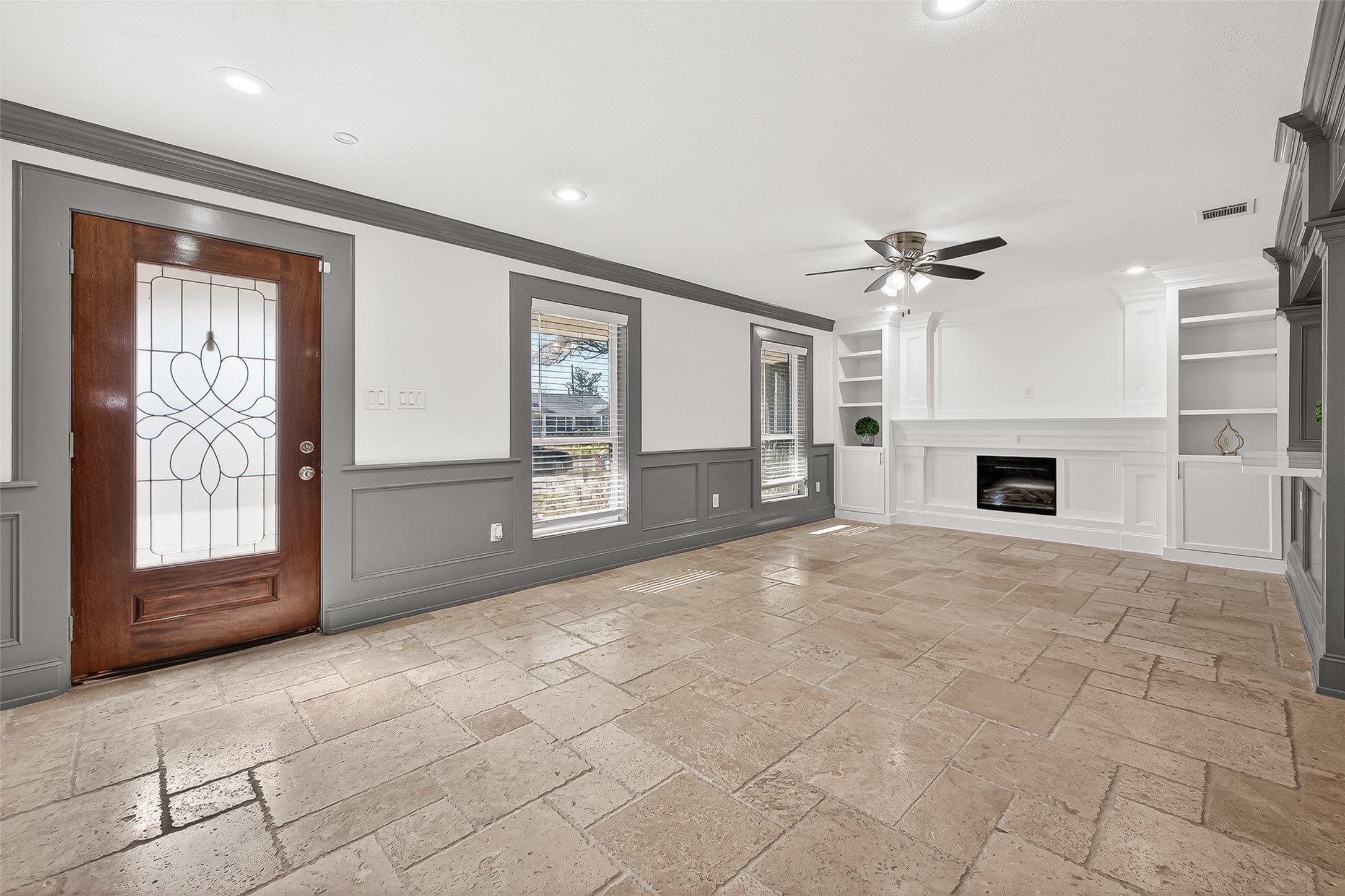 Living room with tiled flooring, a stylish wooden door, and large windows.
