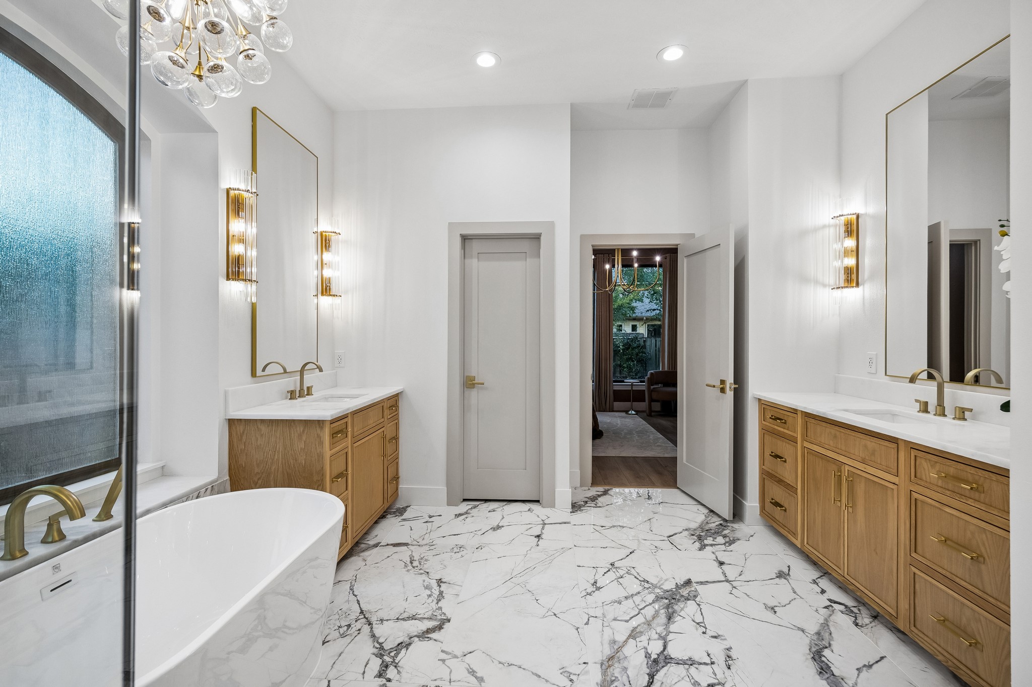Primary bathroom features porcelain tile flooring, white oak cabinetry, a freestanding tub, designer fixtures and sconces