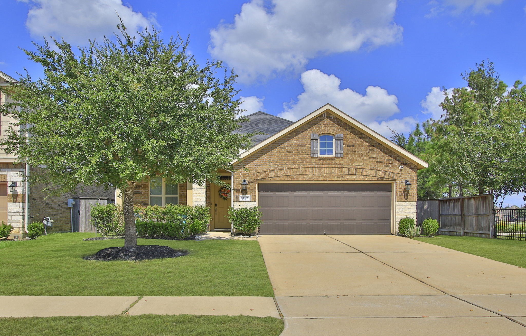 Charming brick home with a spacious two-car garage and a beautifully landscaped front yard featuring a mature tree.