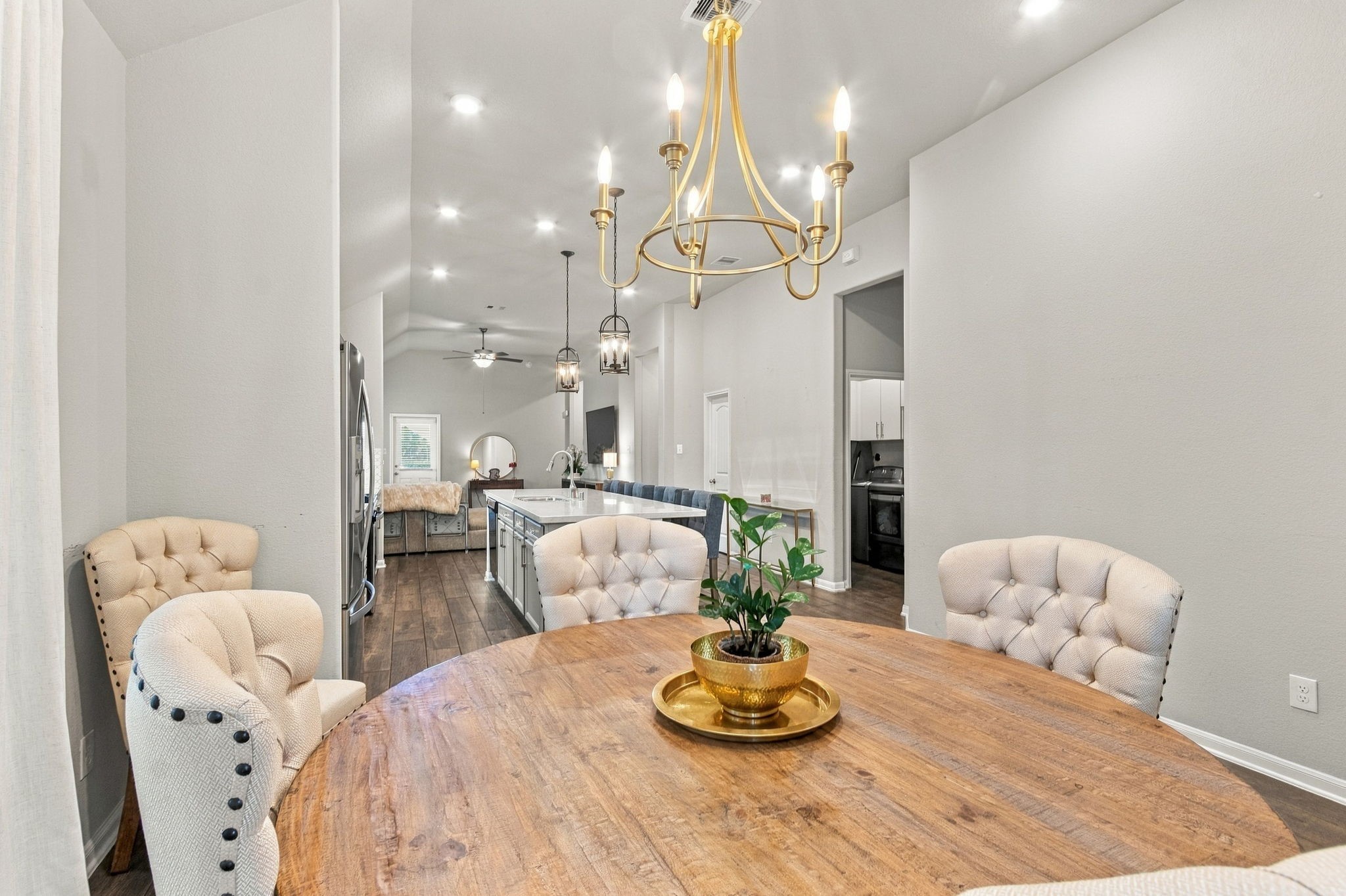 Elegant dining area complemented by a stylish chandelier overhead. Open floor plan extends to a modern kitchen with sleek finishes and a cozy living space beyond.