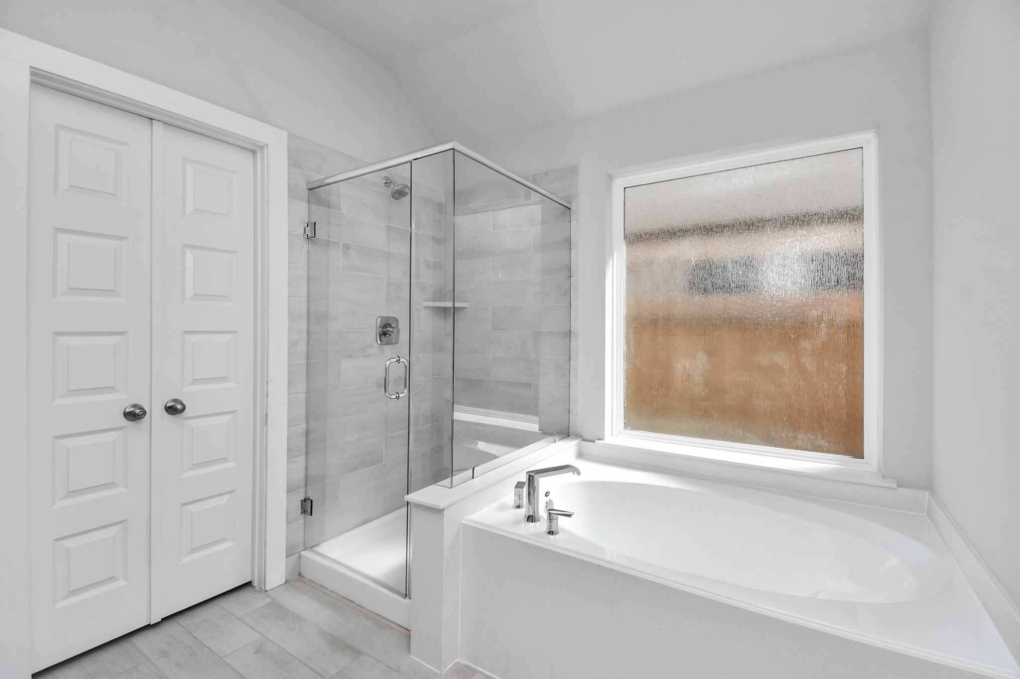 Indulge in a spa-like retreat within the confines of this primary bathroom. Delight in a spacious walk-in shower enveloped in stylish tile surround and unwind in a separate garden tub adorned with custom detailing. Sample photo of completed home with similar floor plan. Actual colors and selections may vary.