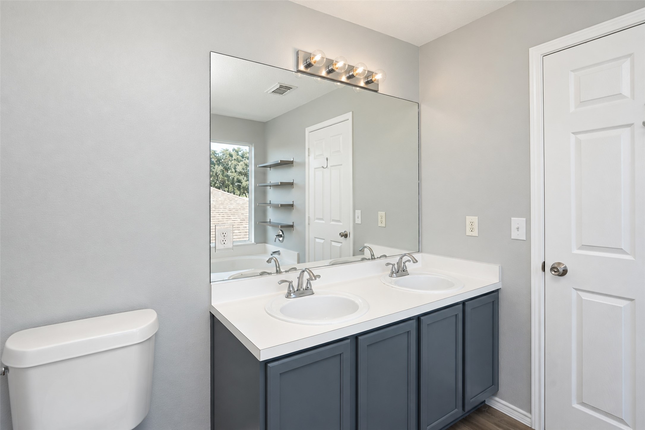 Elegant primary bathroom featuring a double vanity with sleek faucets, a large mirror, and modern lighting.