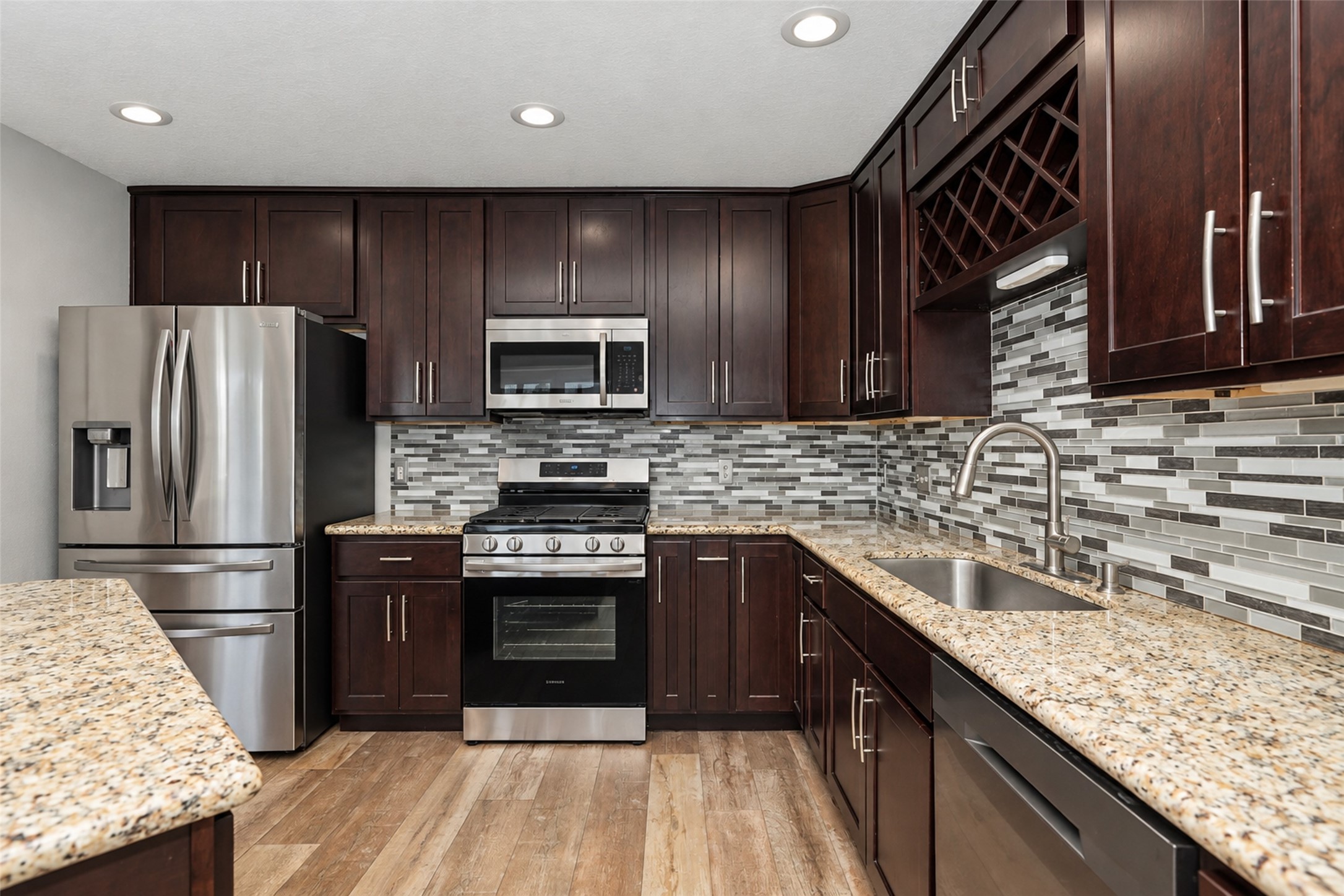 Modern kitchen featuring rich dark wood cabinetry, a stylish mosaic tile backsplash, and sleek granite countertops.