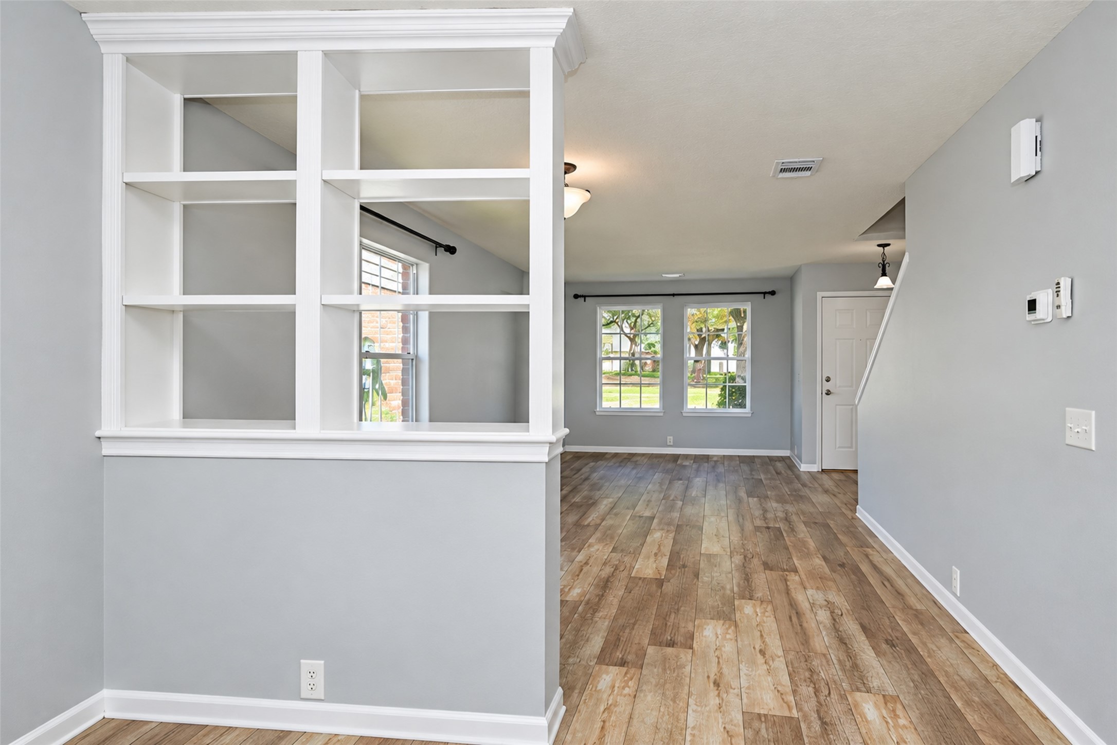 Spacious open-concept living area with elegant built-in shelving, abundant natural light from large windows, and stylish wood-look flooring. Spacious open-concept living area with elegant built-in shelving, abundant natural light from large windows, and stylish wood-look flooring.