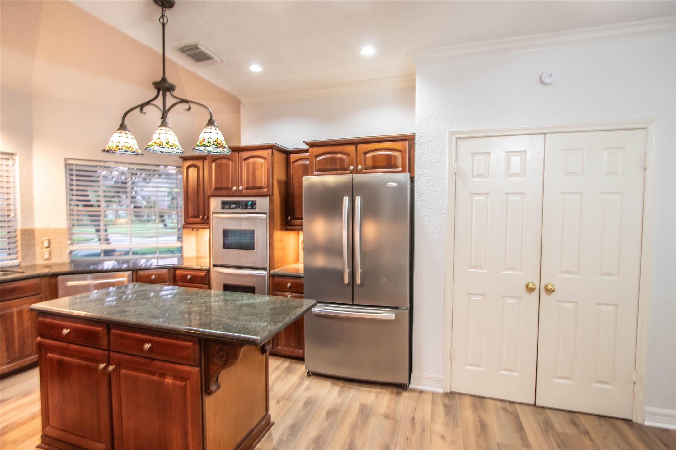The right side of the kitchen with double ovens, a refrigerator, table island and the pantry.