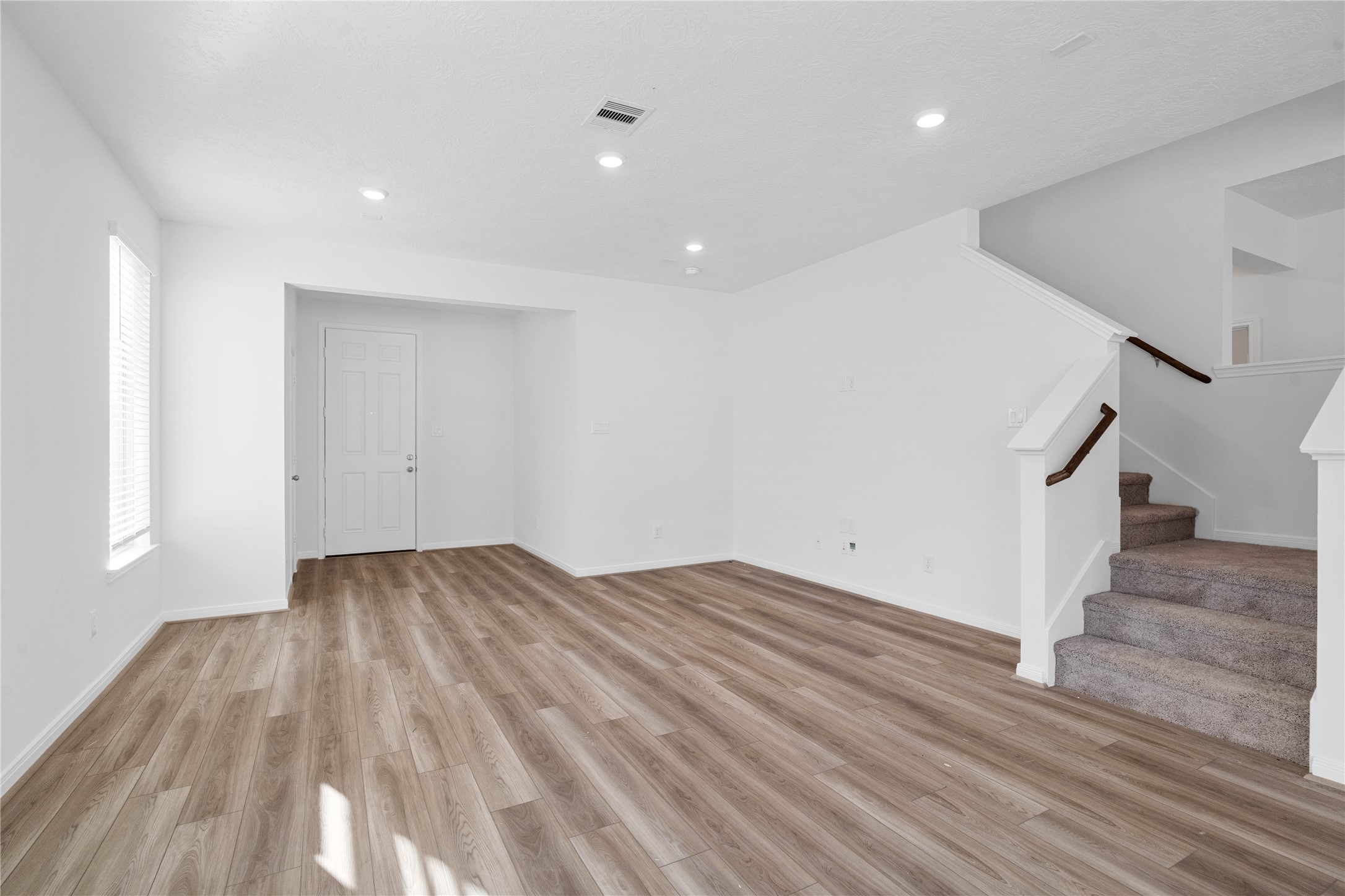 The spacious living room features warm wood look flooring, recessed lighting, and large windows that fill the space with natural light. Its open layout creates a comfortable setting for relaxing or gathering with family and friends.