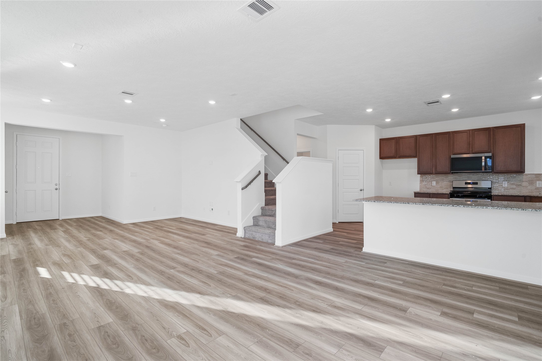 Enjoy an inviting main living area with modern wood look flooring, bright neutral finishes, and an abundance of natural light. The open concept design flows seamlessly toward the kitchen and dining area, making everyday living and entertaining feel effortless.