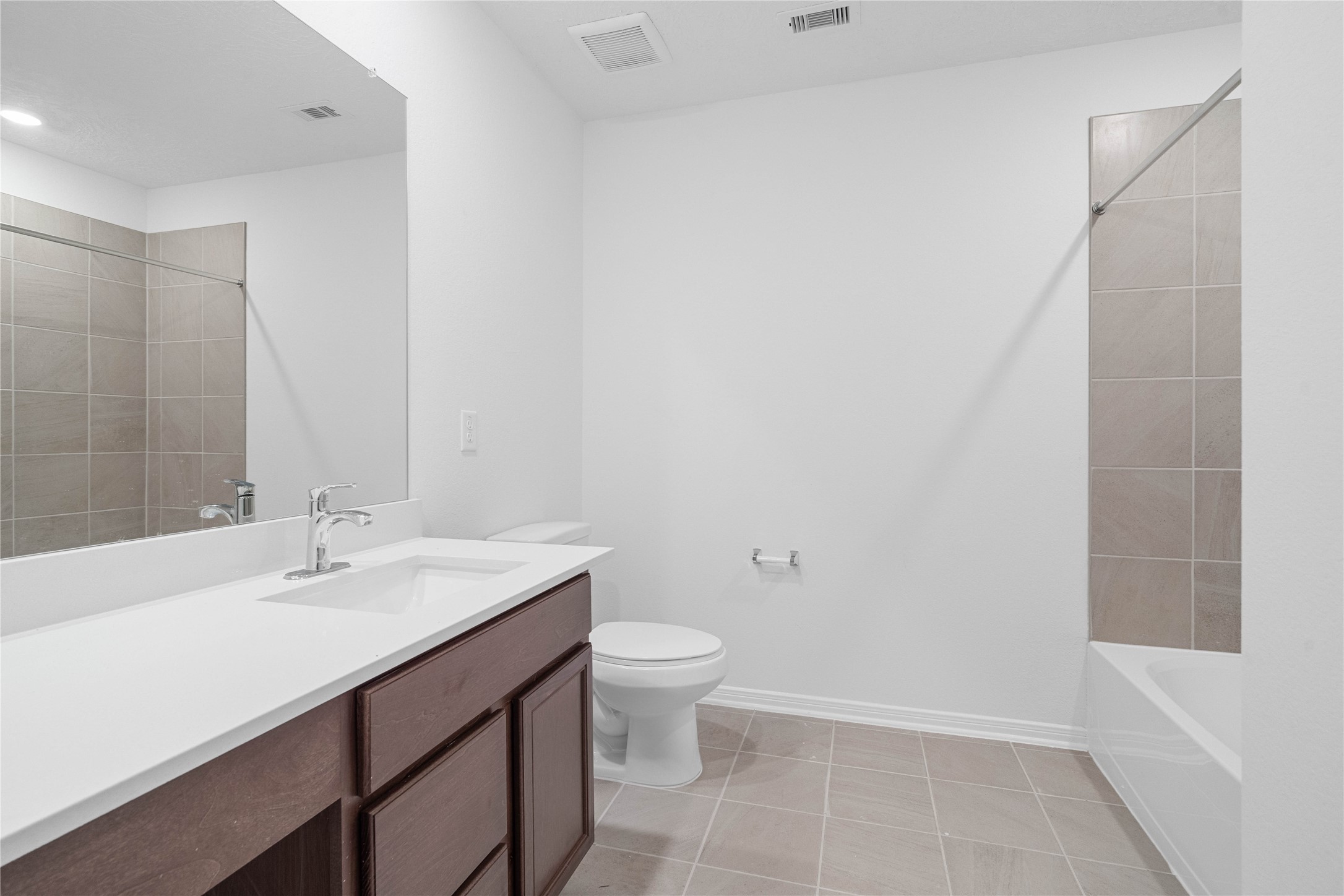 The shared family bathroom features a rich wood vanity, crisp white countertop, and neutral tile flooring for a clean, modern look. A tiled tub and shower combination adds everyday functionality for family and guests.