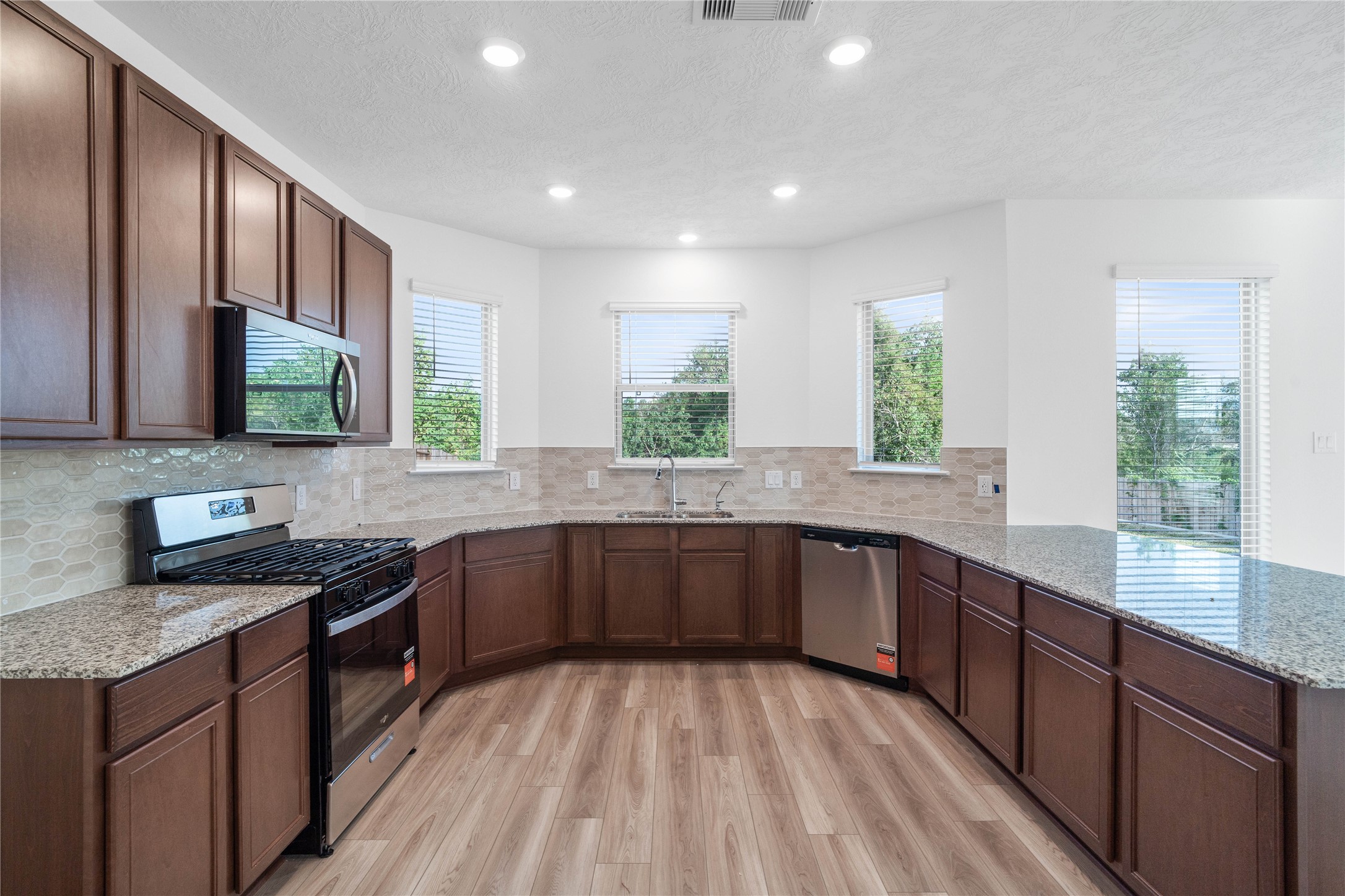 Designed for both style and functionality, this kitchen offers abundant cabinetry, generous granite countertop space, and a convenient wraparound layout. Whirlpool appliances, a soft neutral backsplash, and warm wood look flooring complete the polished look.