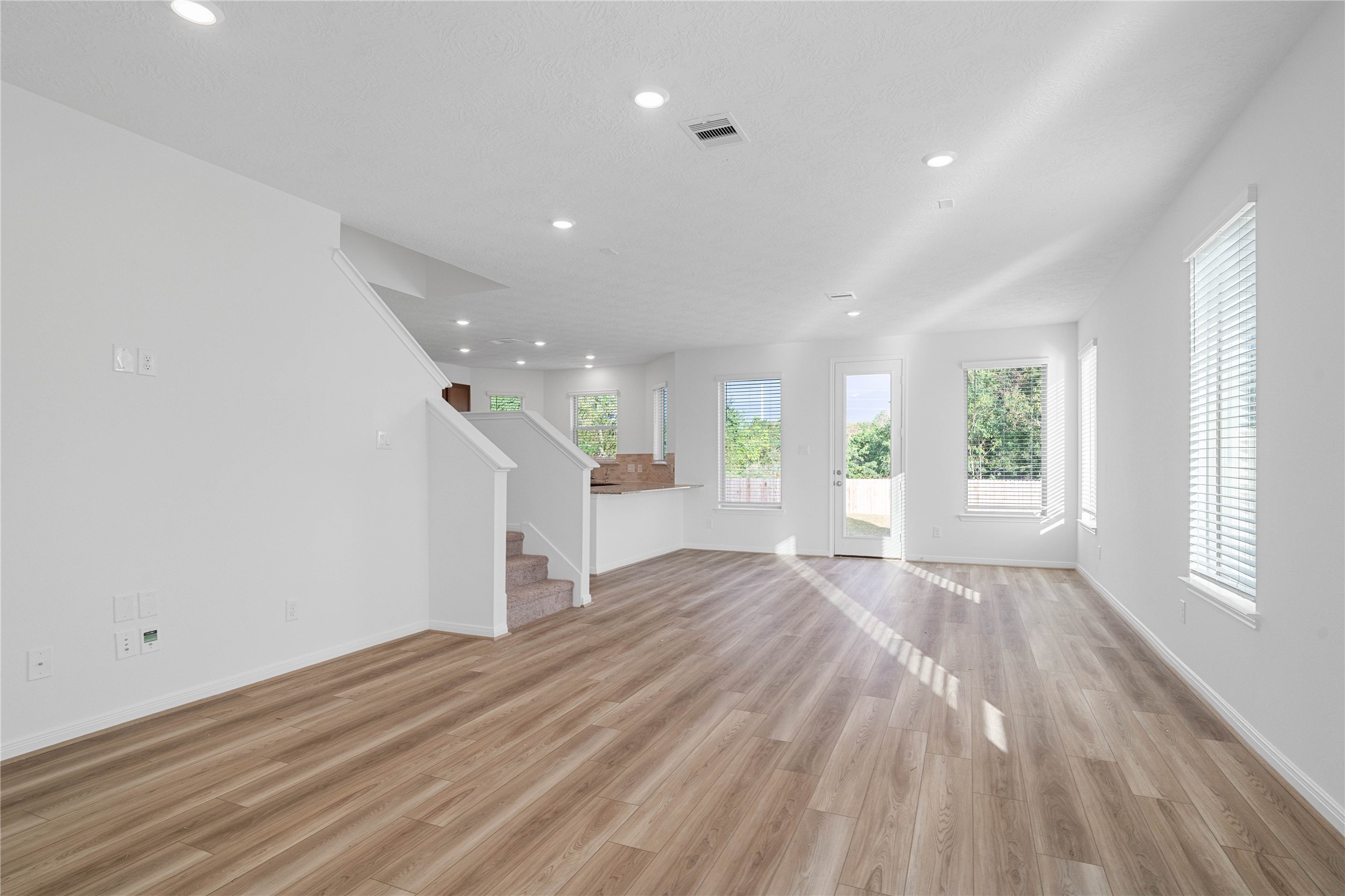 Step inside to a bright, welcoming interior with warm wood look flooring, crisp white walls, and recessed lighting throughout. The open living space and convenient access to the staircase create a functional layout with a clean, contemporary feel.