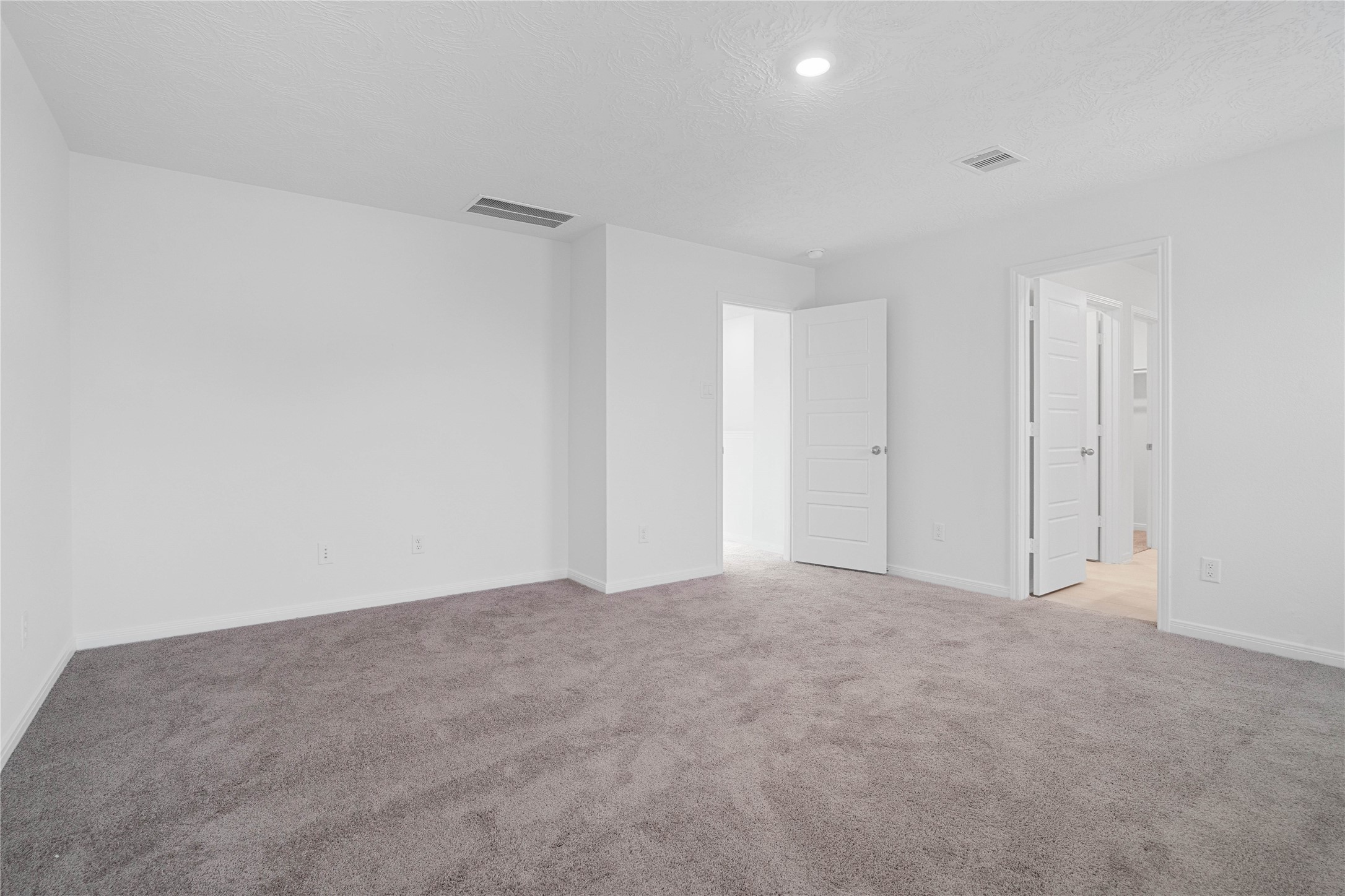 The primary bedroom offers a spacious retreat with soft gray carpeting, crisp white walls, and recessed lighting for a clean, contemporary feel. The neutral palette makes it easy to personalize the space and create a relaxing place to unwind.