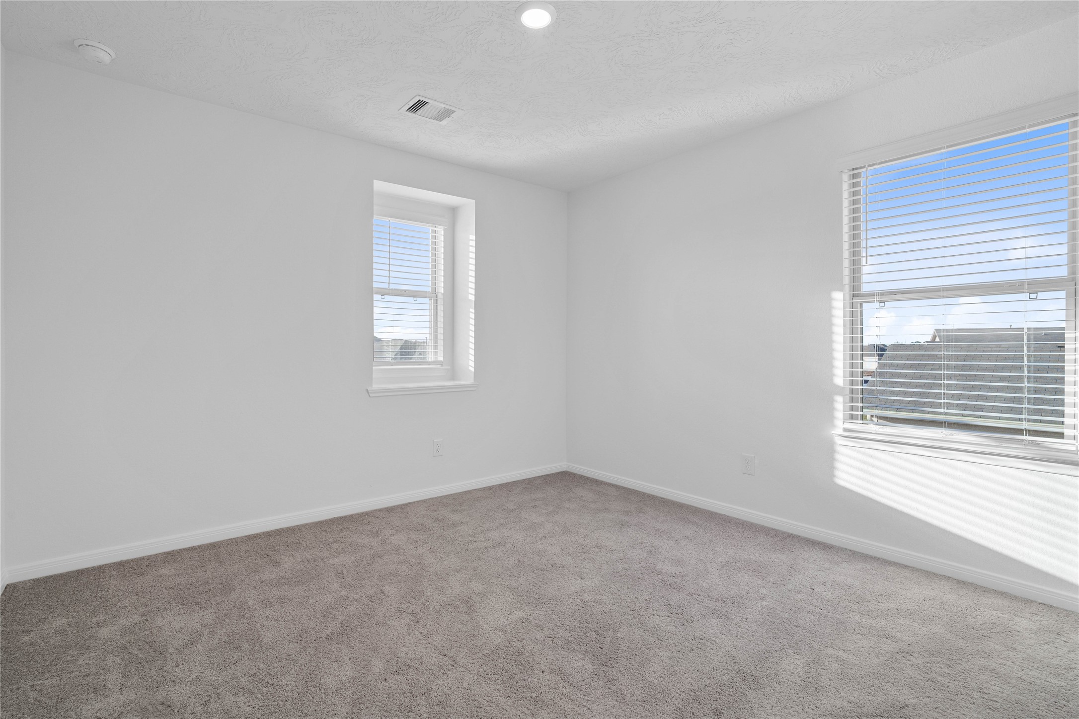 This upstairs bedroom features soft gray carpeting, neutral walls, and a bright, comfortable atmosphere. Its versatile layout makes it ideal for family, guests, or a personal home office.