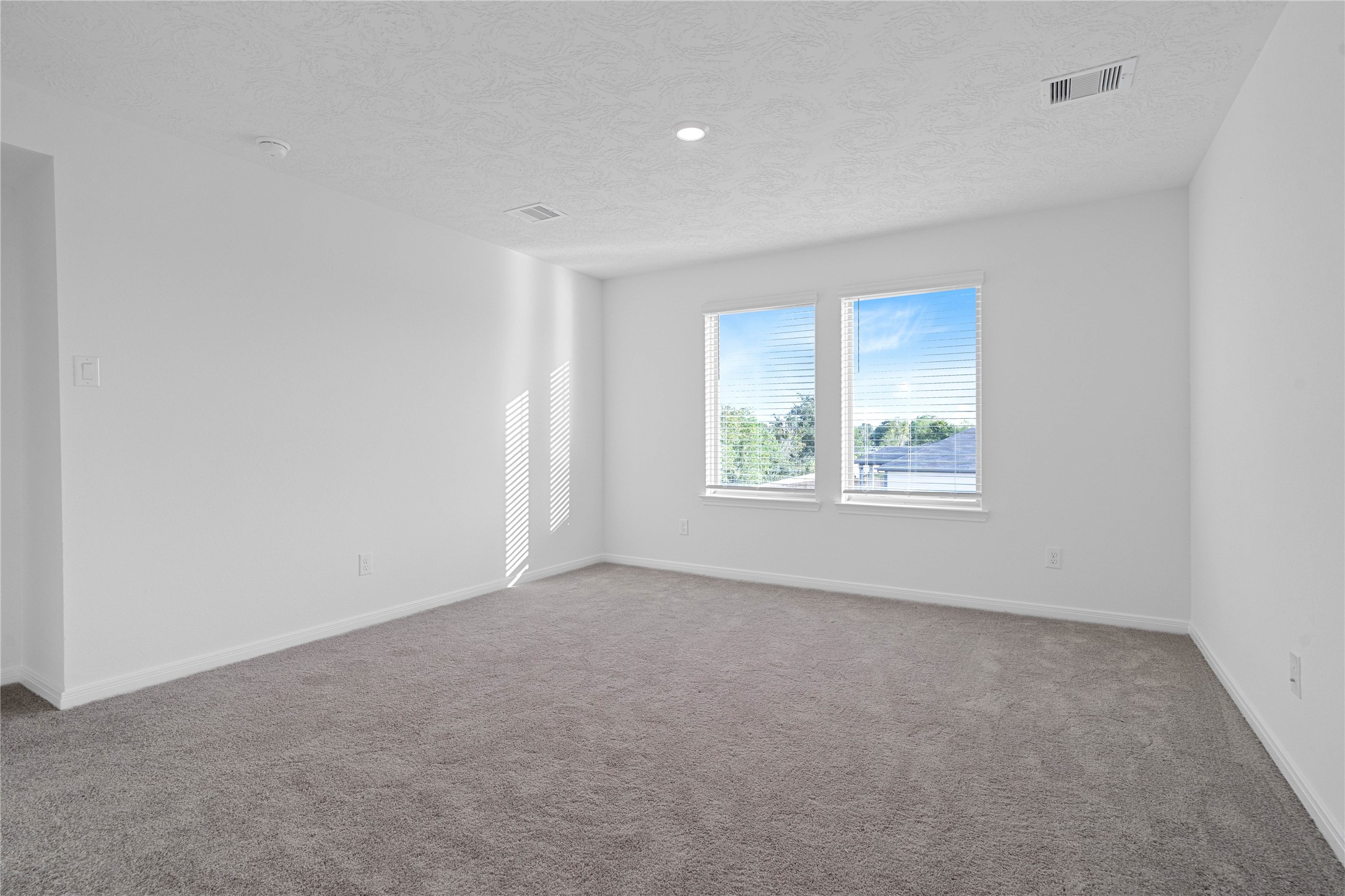 The upstairs loft offers a versatile bonus space with soft gray carpeting, neutral walls, and natural light from the surrounding windows. Make it your own as a cozy second living area, game room, or home office.