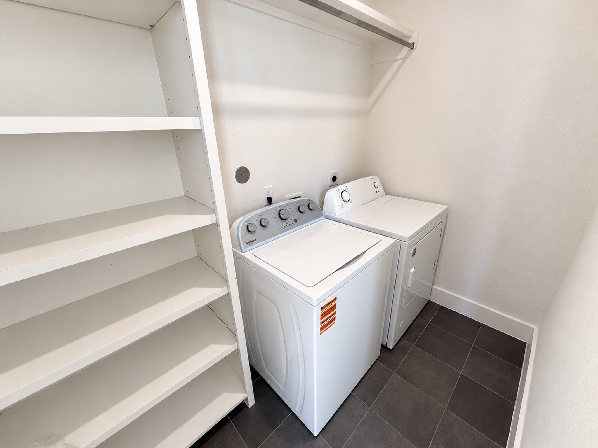 Convenient third-floor laundry room with a washer, dryer, and built-in storage shelves.