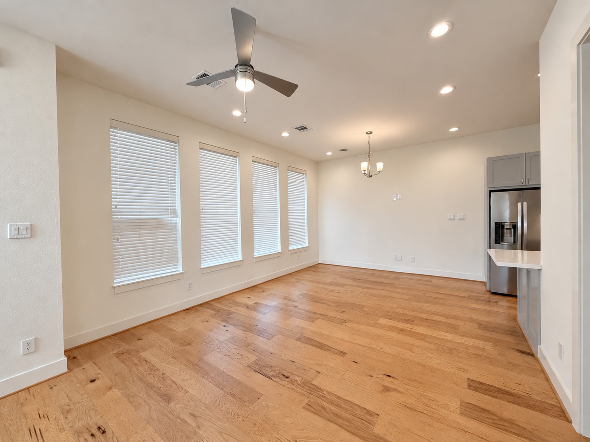 Bright, open living room featuring wood floors, abundant windows, and seamless flow into the kitchen and dining area.