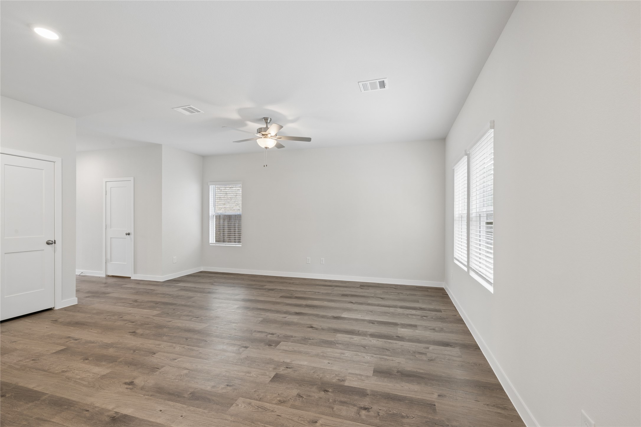 Spacious living area with elegant wood flooring, abundant natural light, and a modern ceiling fan, perfect for relaxation or entertaining. Spacious living area with elegant wood flooring, abundant natural light, and a modern ceiling fan, perfect for relaxation or entertaining.
