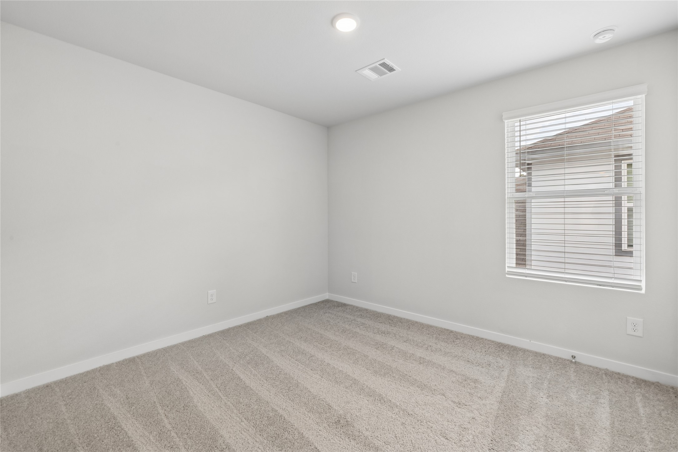 Bright and inviting bedroom with soft carpet flooring, neutral walls, and ample natural light from the window.