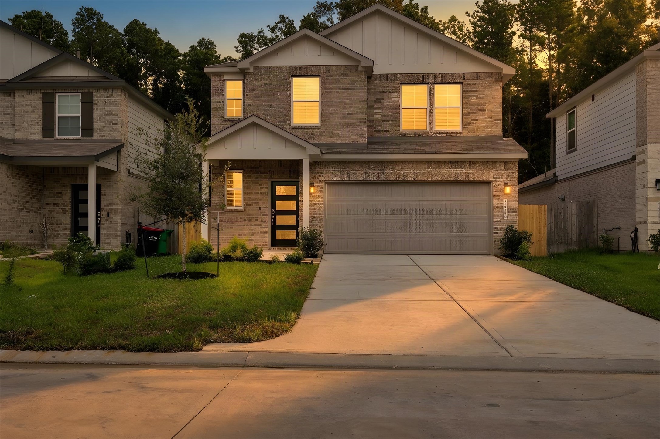 Beautiful two-story brick home with a spacious driveway and attached garage, set against a backdrop of mature trees. Warm interior lighting creates an inviting atmosphere. Beautiful two-story brick home with a spacious driveway and attached garage, set against a backdrop of mature trees. Warm interior lighting creates an inviting atmosphere.