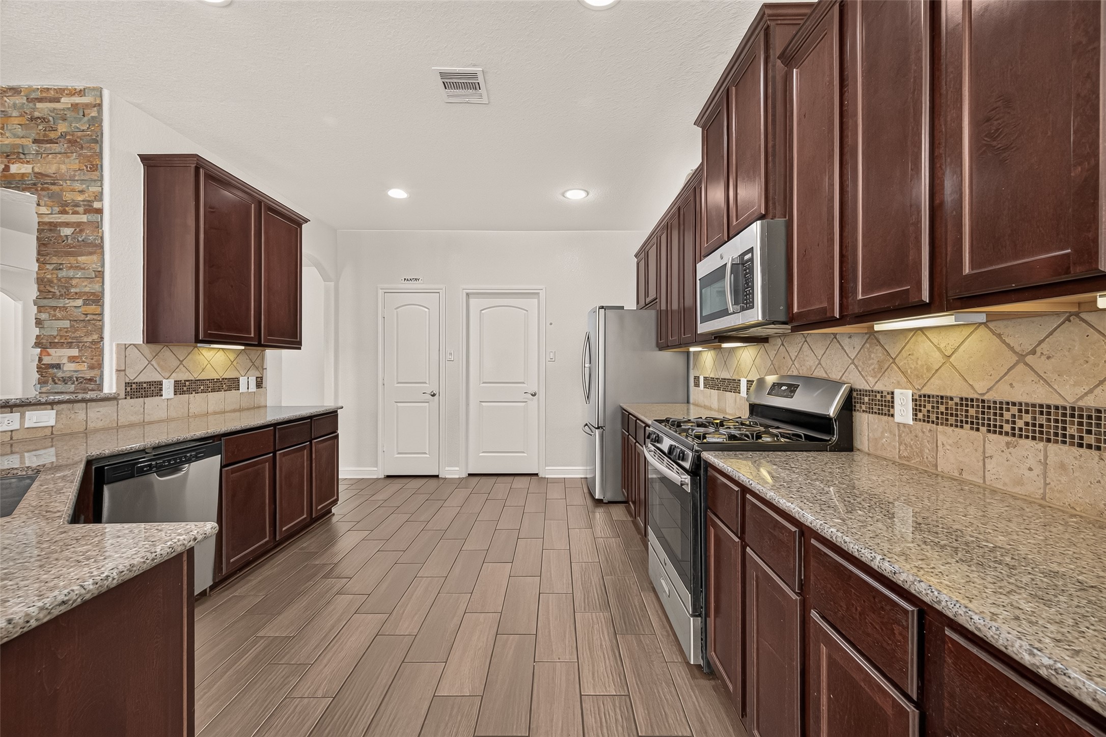 Spacious kitchen with rich wood cabinetry, sleek granite countertops, and modern stainless steel appliances, accented by a stylish tile backsplash and flooring.