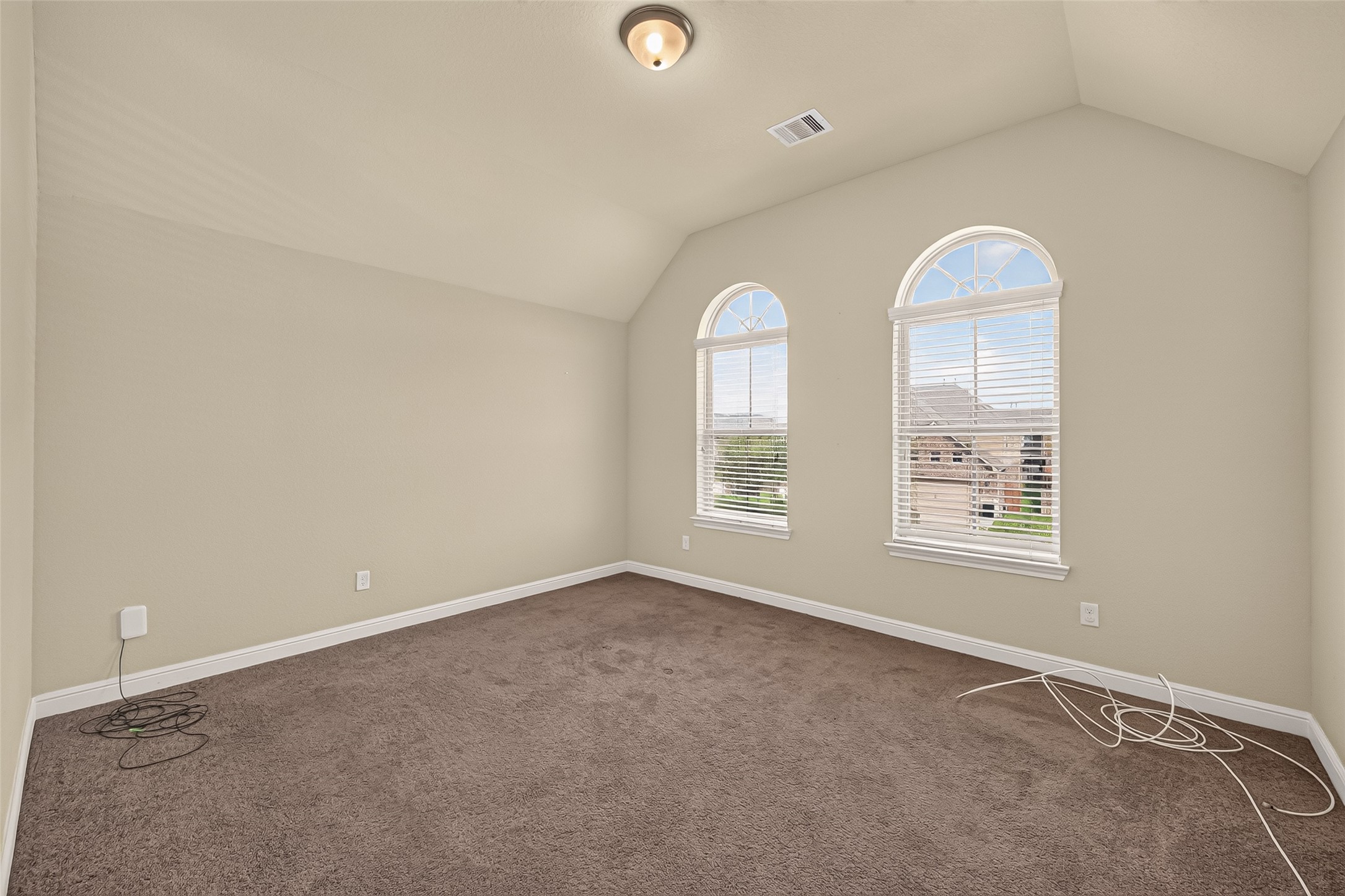 Spacious room with vaulted ceilings and charming arched windows that provide abundant natural light, ideal as a cozy retreat or sixth bedroom with an armoire.