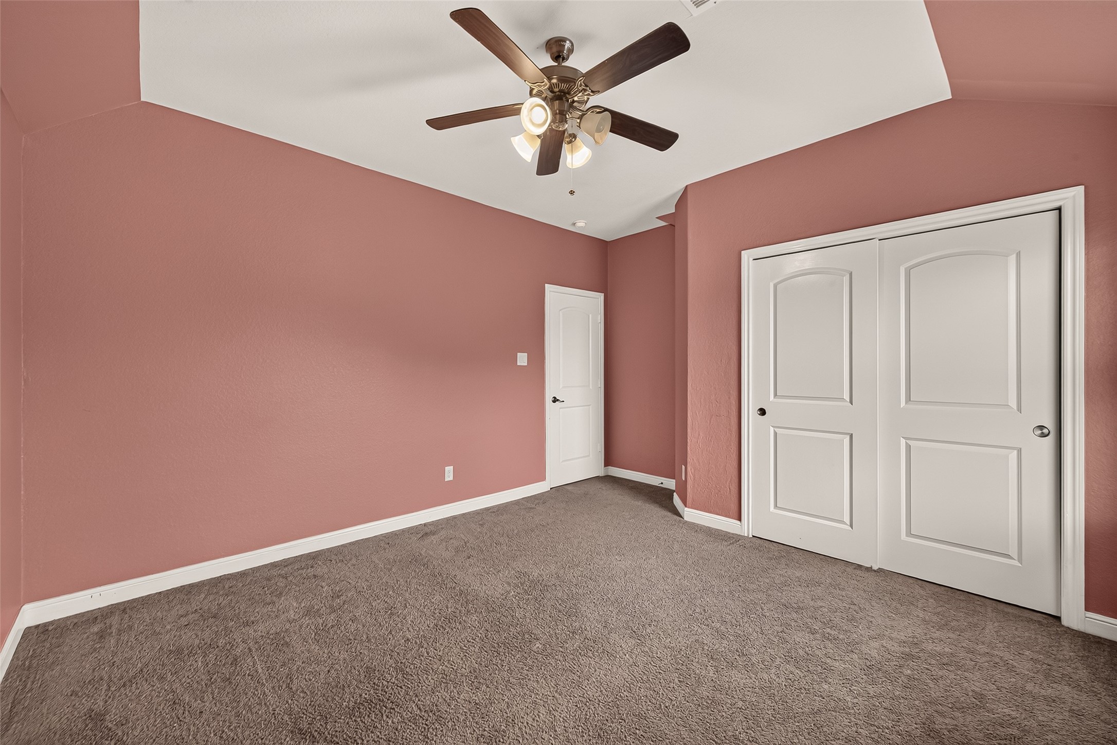 Charming fourth bedroom featuring soft pink walls, plush carpeting, a stylish ceiling fan, and generous closet space with elegant white sliding doors.