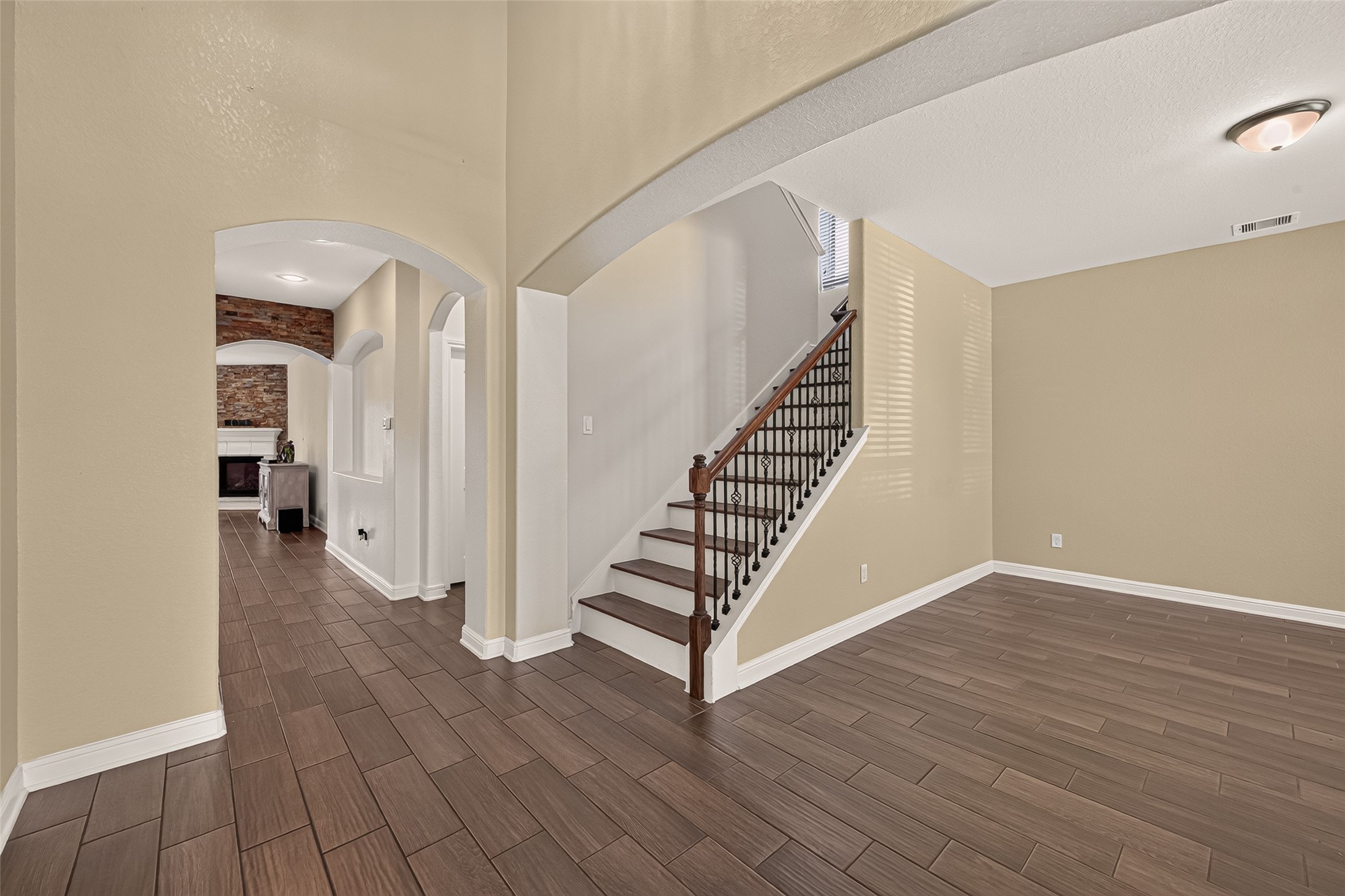 Elegant entryway featuring rich wood-look tile flooring and graceful archways, leading to a charming staircase with decorative iron balusters.