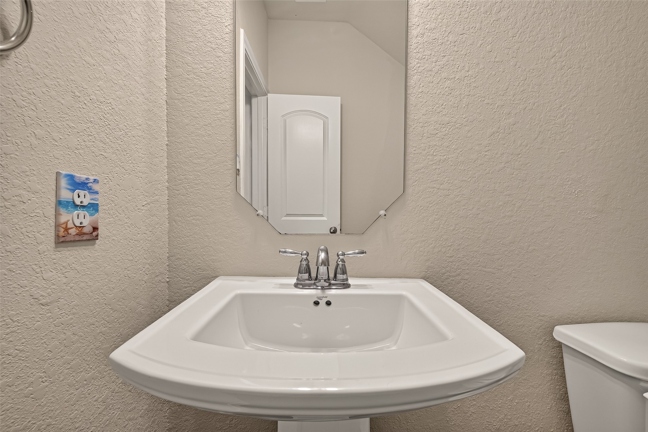 Charming powder room with a sleek pedestal sink, elegant mirror, and neutral tones, offering a cozy and functional space.