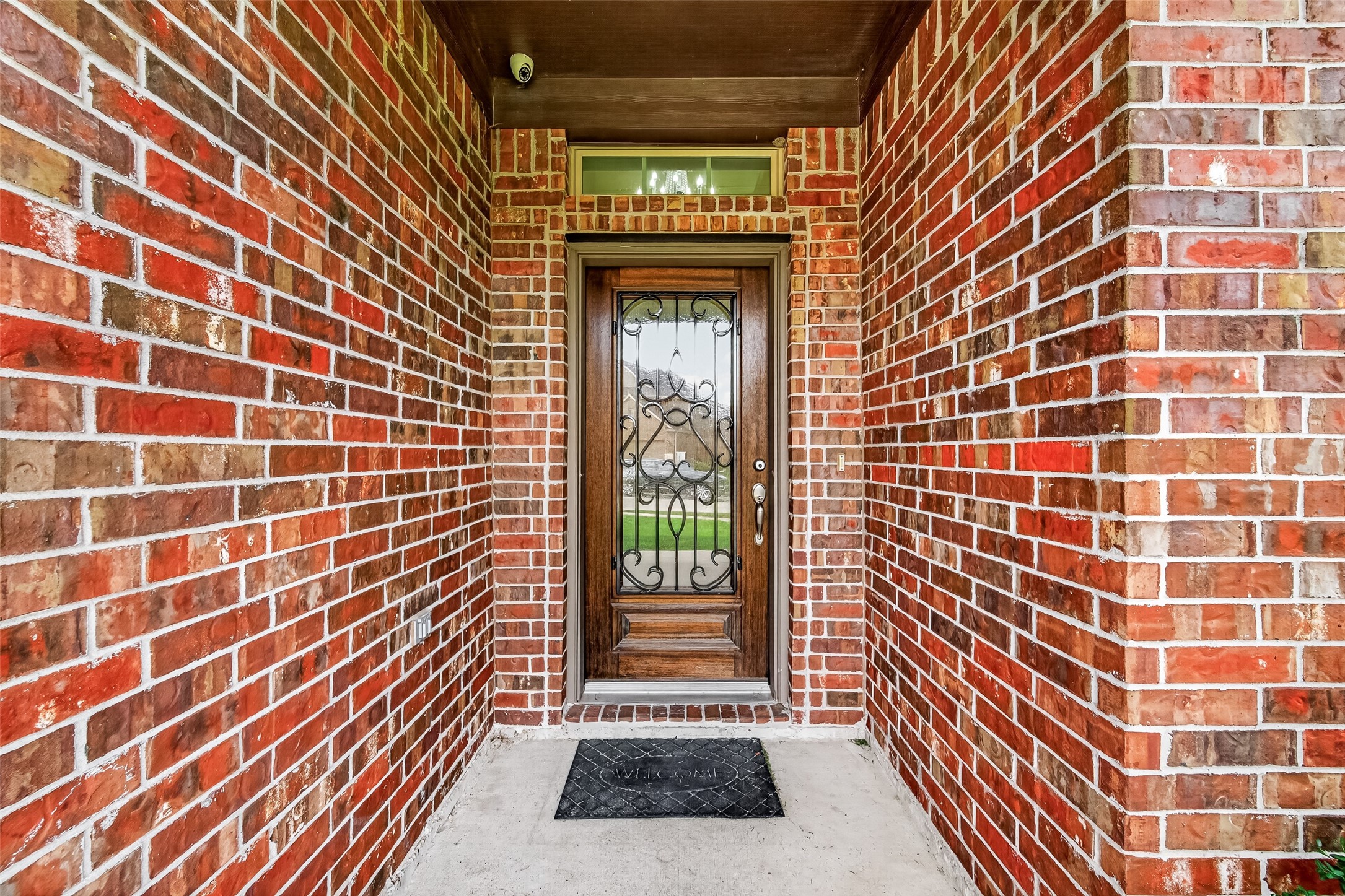 Inviting entrance with a charming wooden door featuring ornate ironwork, set against classic red brick walls.