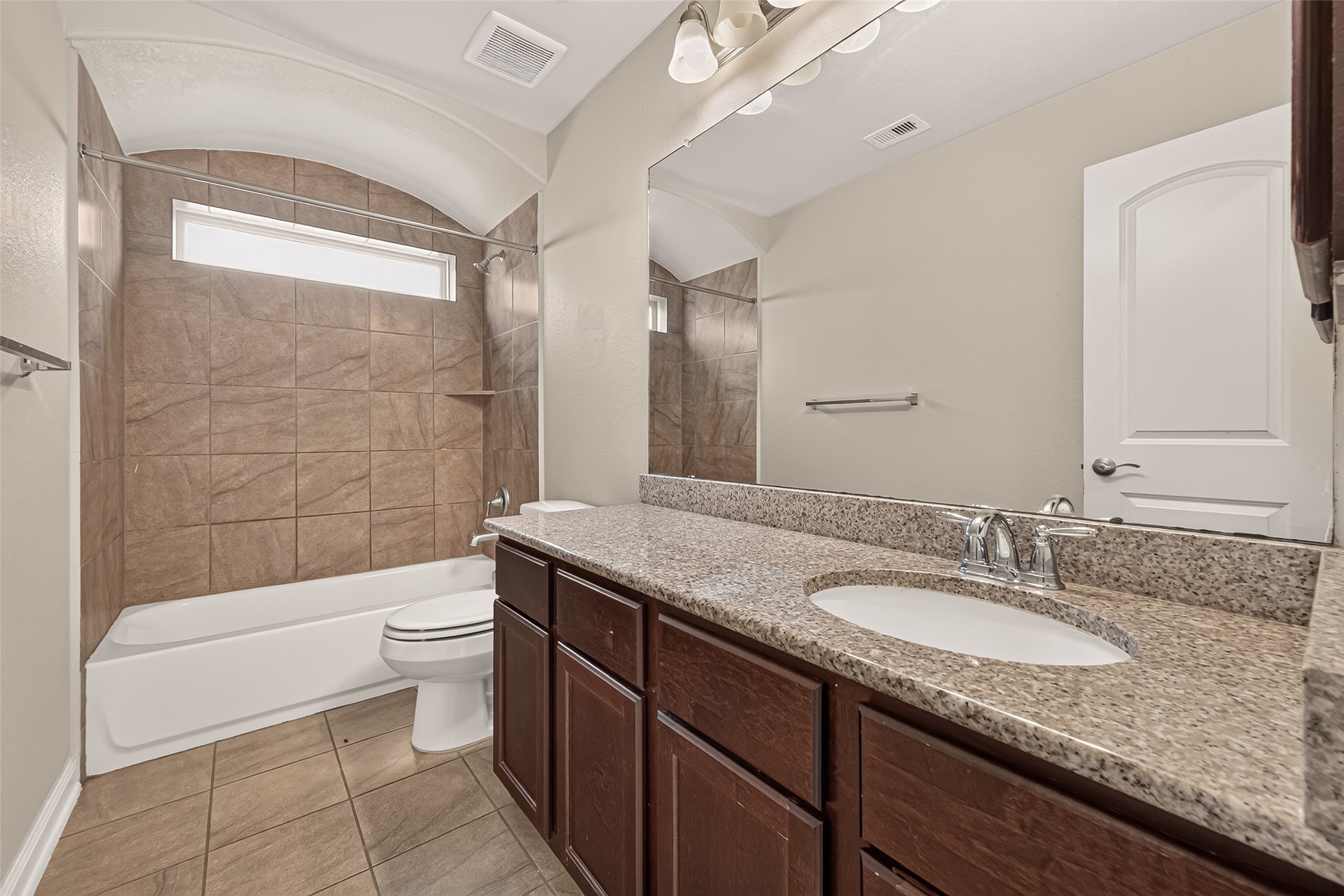 Spacious third bathroom featuring a granite vanity with a porcelain sink, rich dark-wood cabinetry, and an elegant tiled shower.